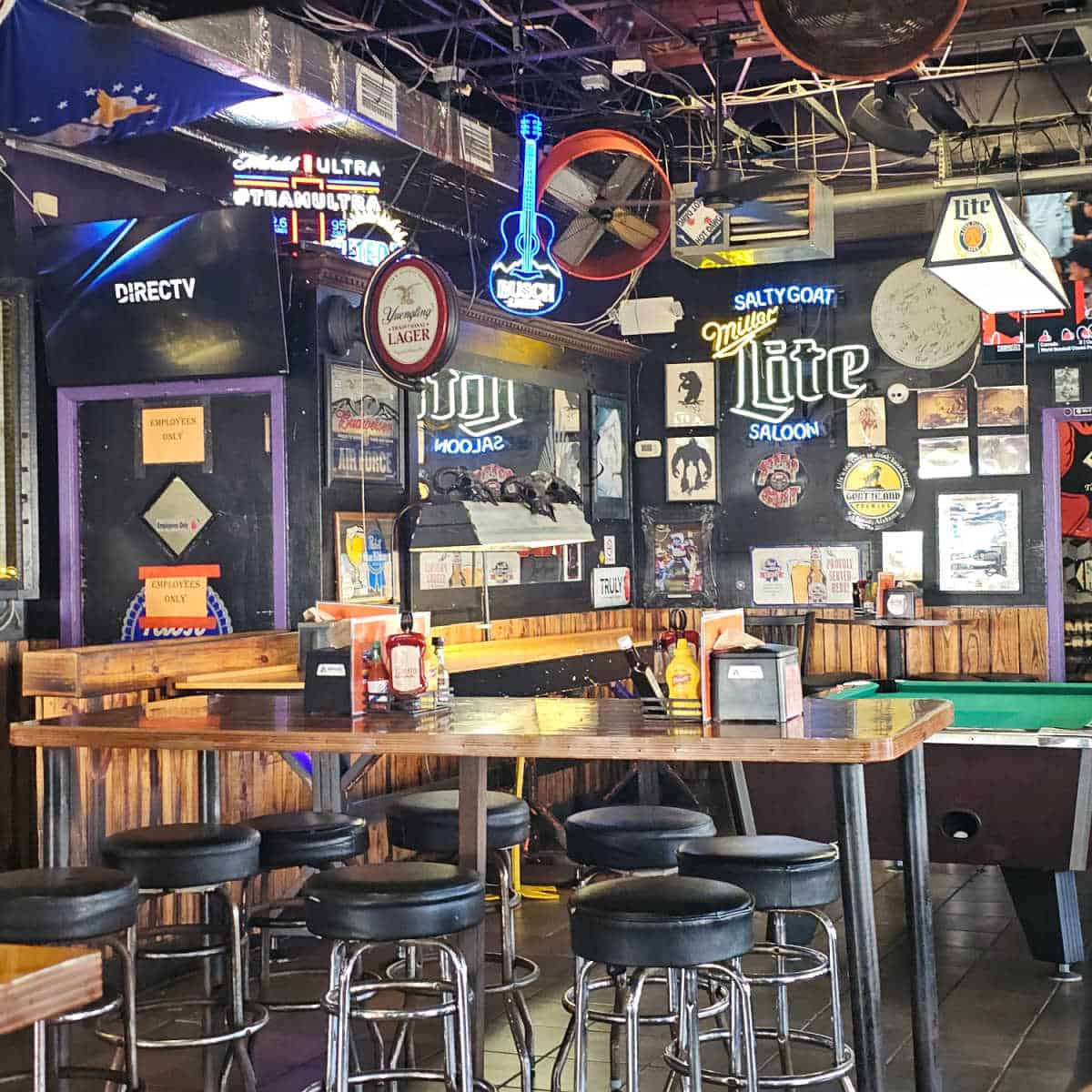 Salty Goat Saloon interior with pool tables, tall tables and bar stools, neon lights and art on the wall