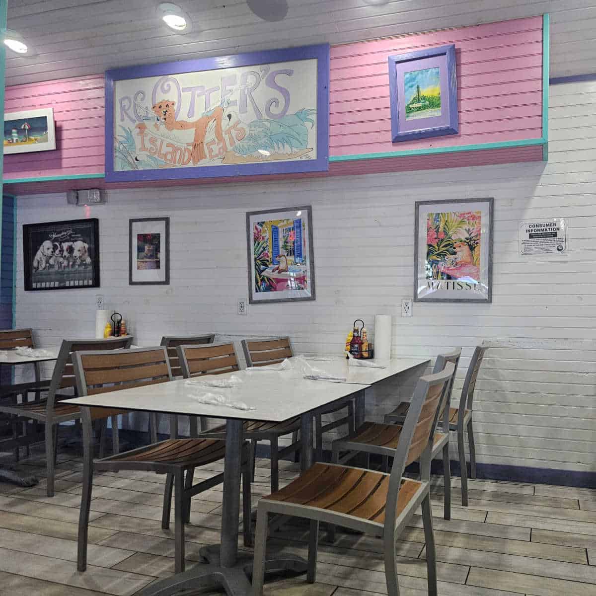 RC Otters Island Eats sign wtih an otter on it on a pink wall above tables and chairs, wall covered in otter and dog art