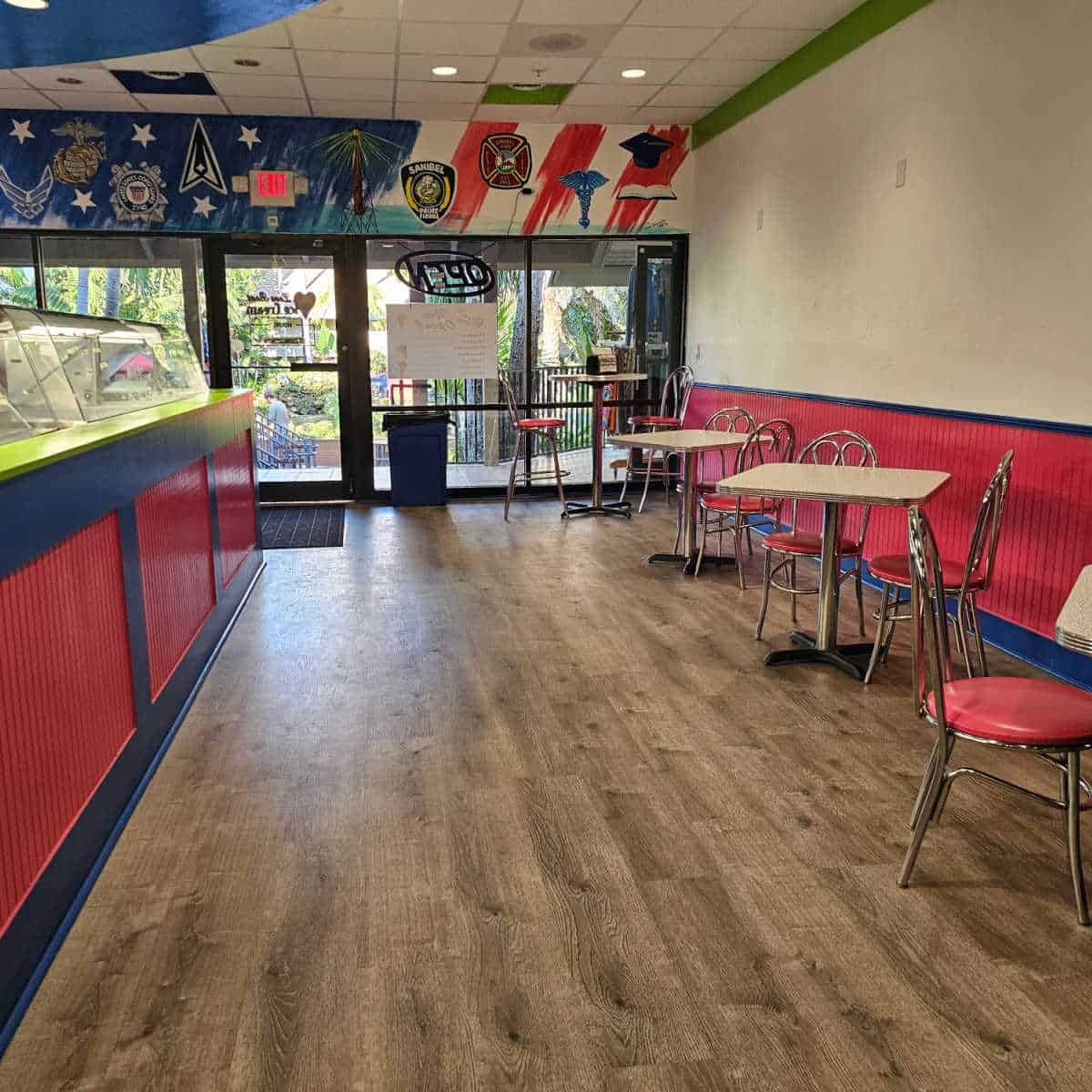 Ice Cream shop table and chairs along one wall, ice cream counter with red and blue wall on the left, military and armed forces logos on the wall by the door