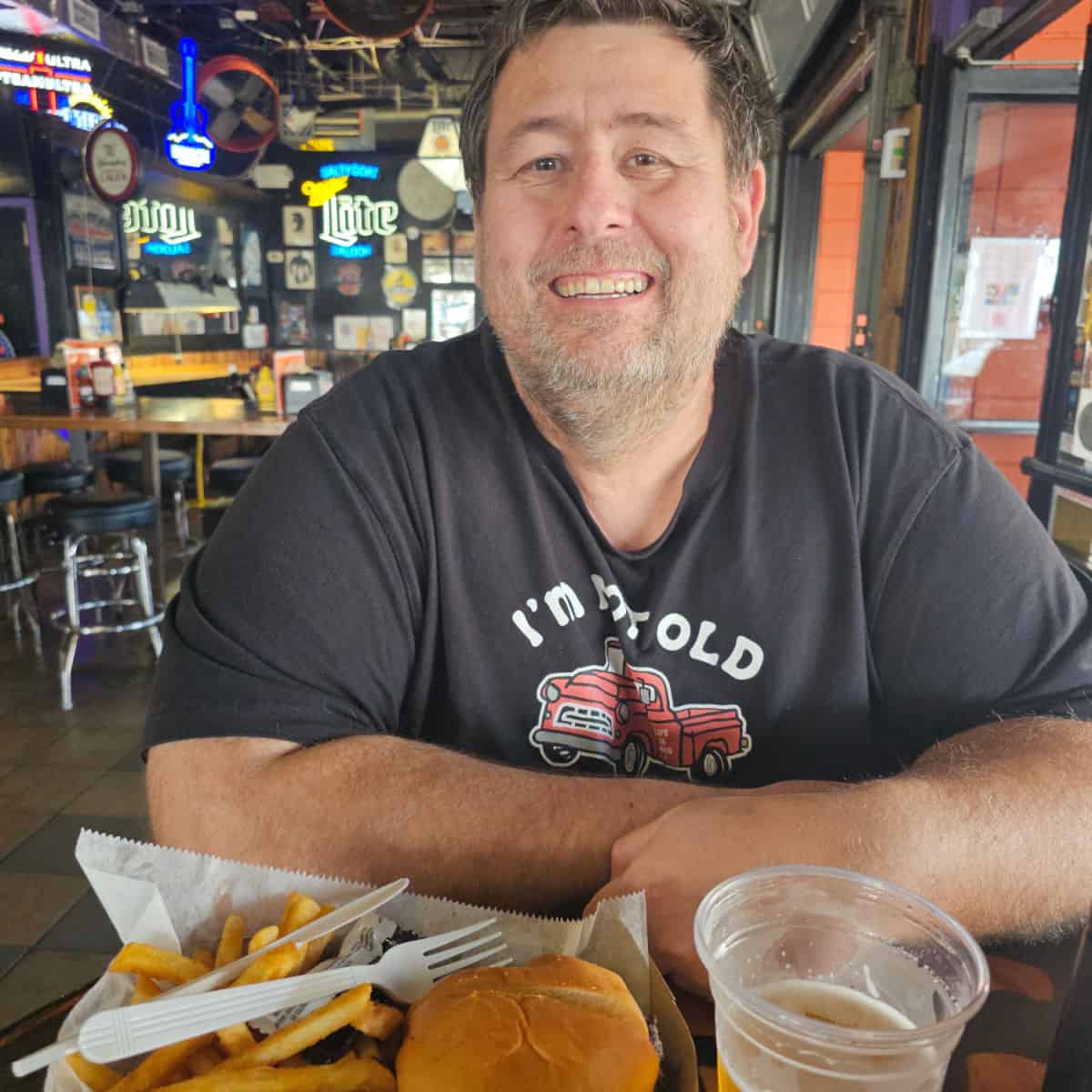 John smiling at a tall table with neon signs and art behind him