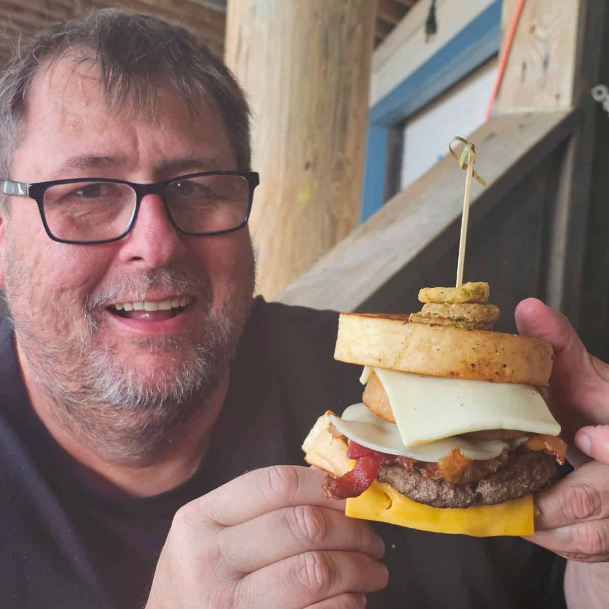 John holding a burger with onion rings and fried pickles on it