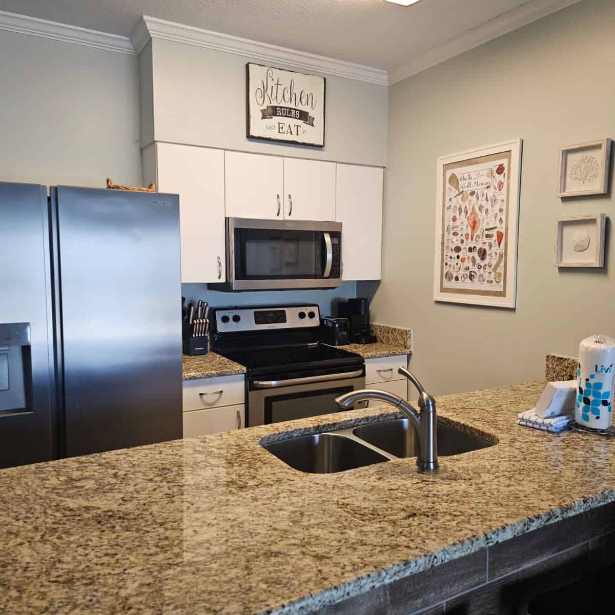 kitchen with grey walls, shell art on the walls, white cabinets, granite counters and stainless steel appliances