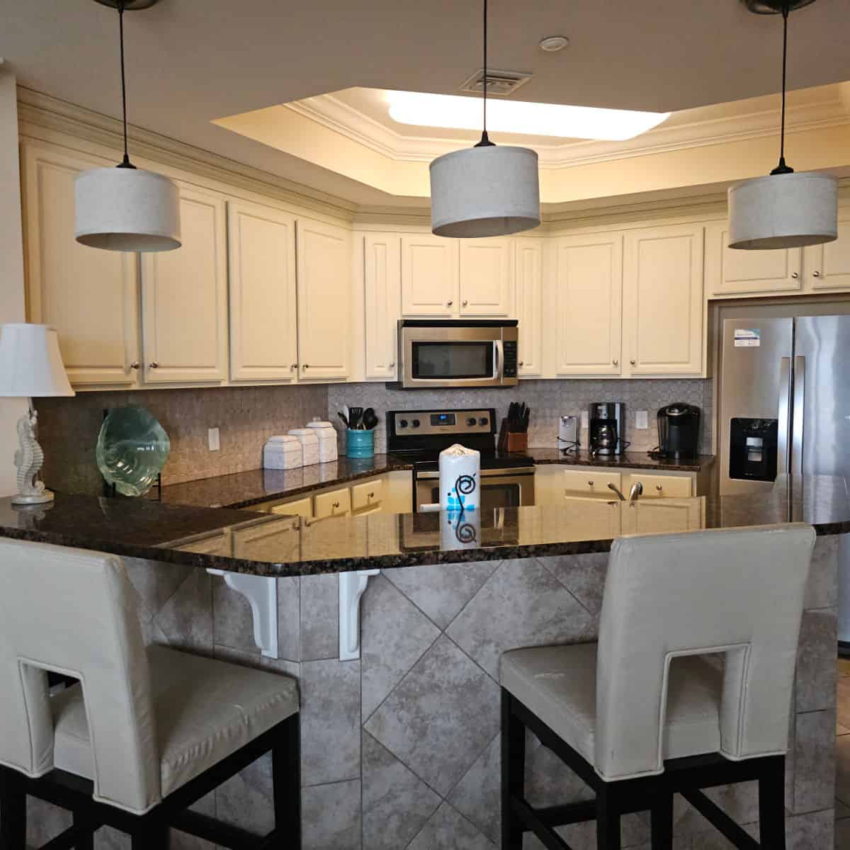 kitchen with cream cabinets, stainless steel appliances, leather stools next to the bar counter, seahorse base lamp