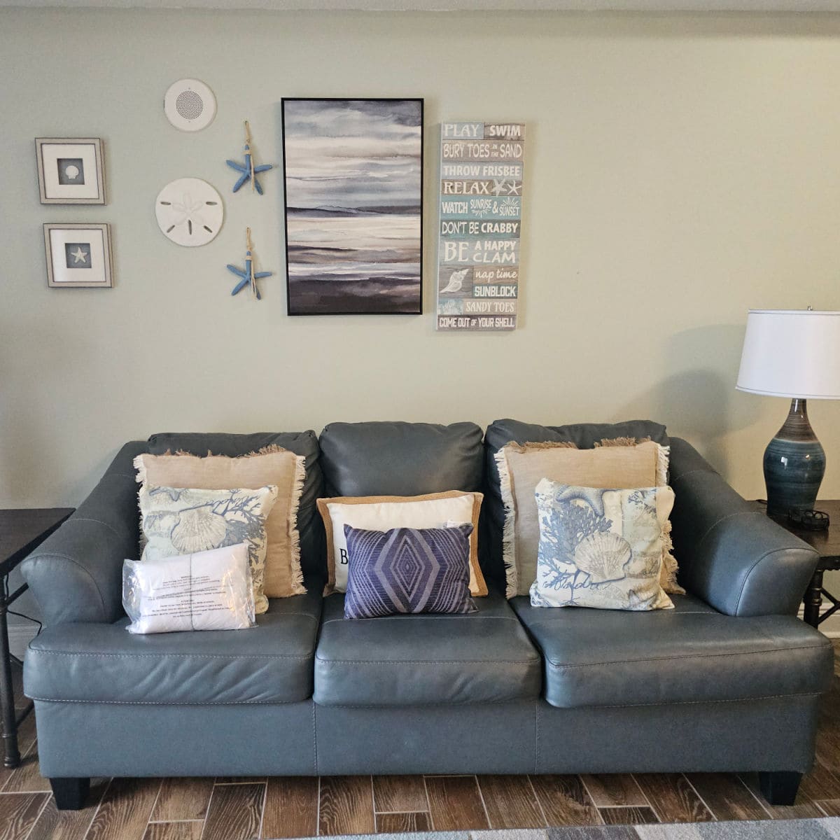 blue leather couch with pillows on it, coastal beach art on the wall with sand dollars and starfish