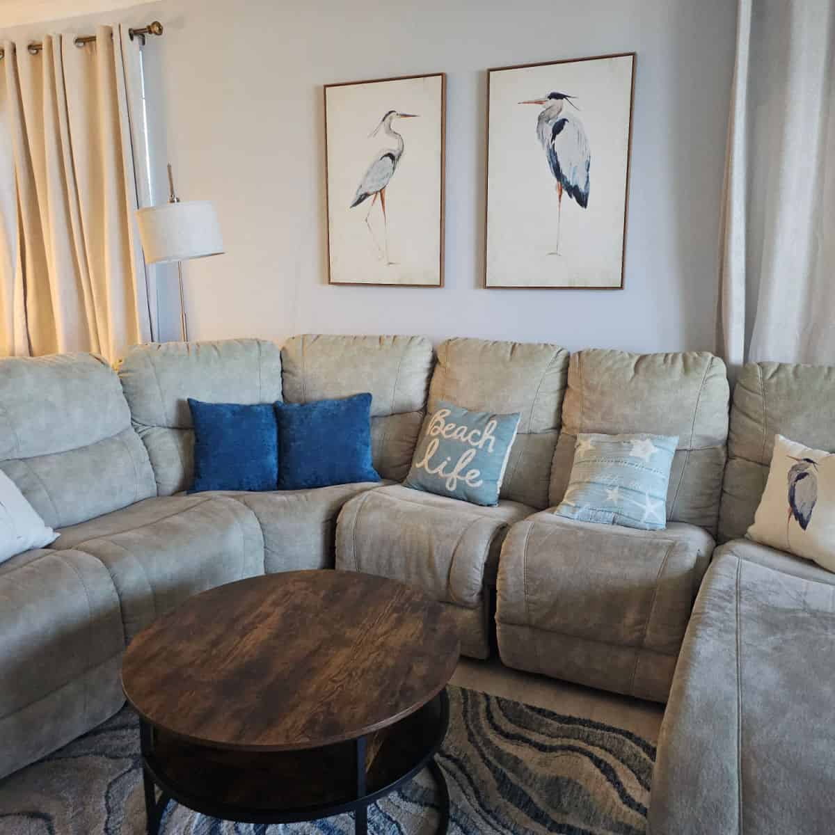 living room area with wrap around grey couch, pillows with beach life and a blue heron on them, wall art with two blue herons