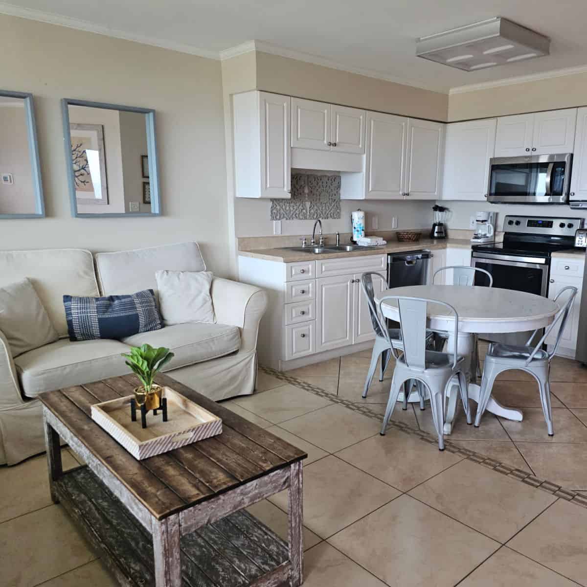 kitchen with white cabinets and stainless steel appliances, white round table with metal chairs, couch with cushions next to a rectangle table