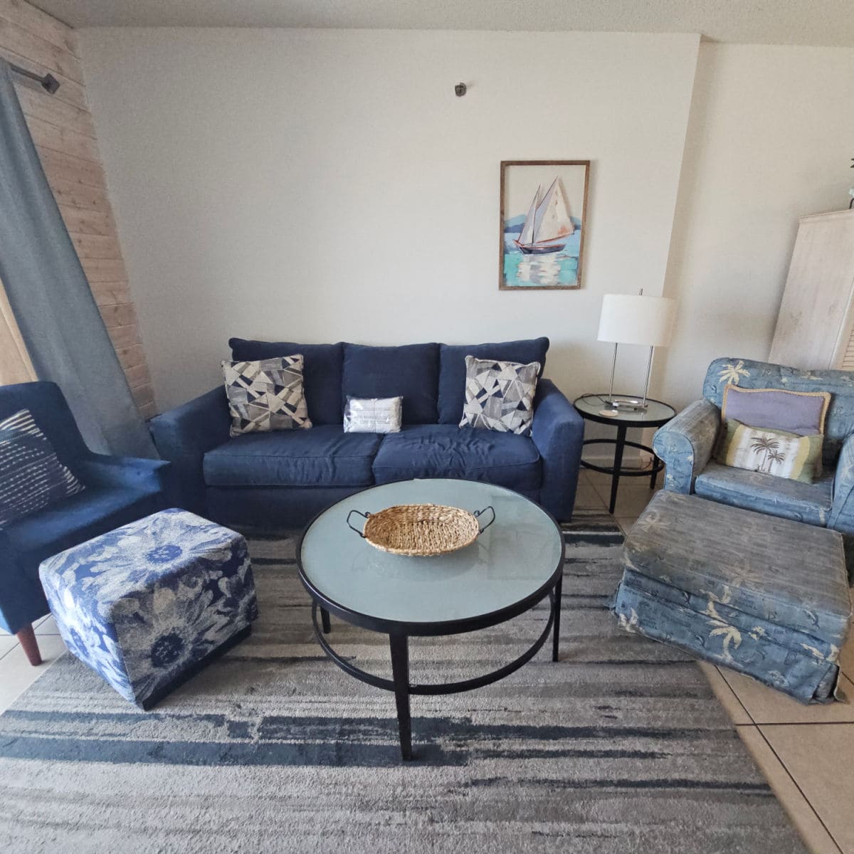 living room with blue couch and blue chairs, coastal pillows, sailboat art on the wall