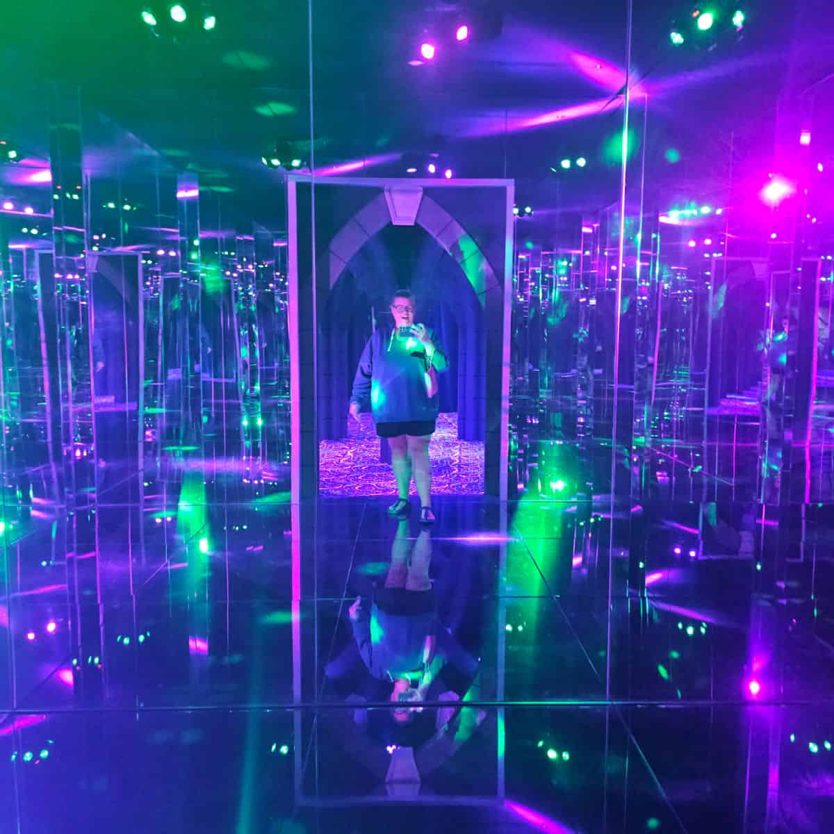 Tammilee in a mirror maze with lights and reflection around her