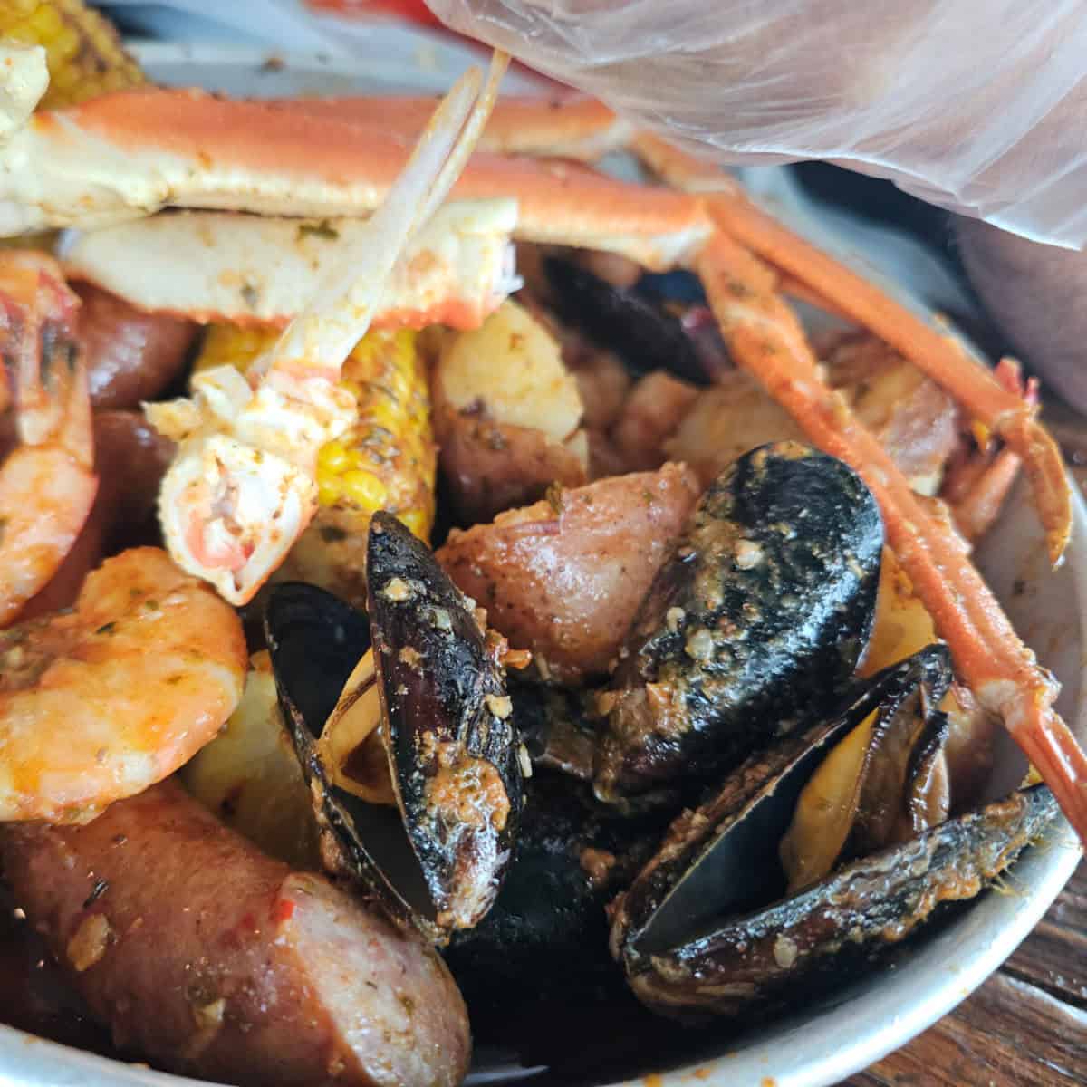 silver bowl with crab legs, mussels, potatoes, corn, and shrimp