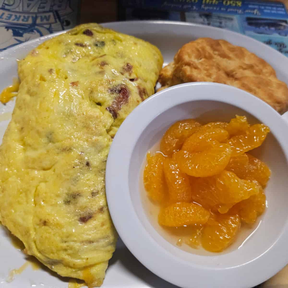 Breakfast plate with omelette, fried item, and fruit in a white dish.