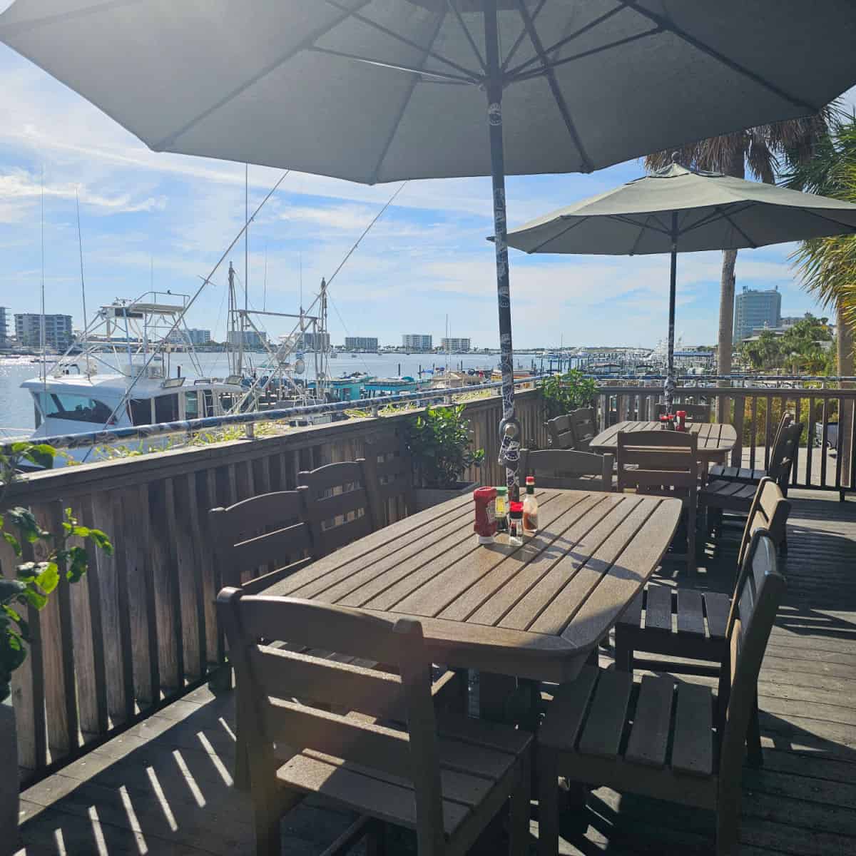 outdoor deck with tables and chairs with umbrellas over the table looking out to boats and the water in Destin