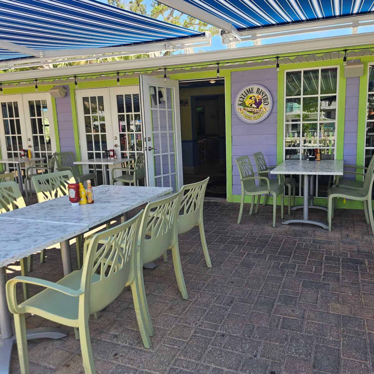 purple building with green trim, Keylime Bistro sing on the wall, tables and chairs outside of the front entrance with a blue cover overhead