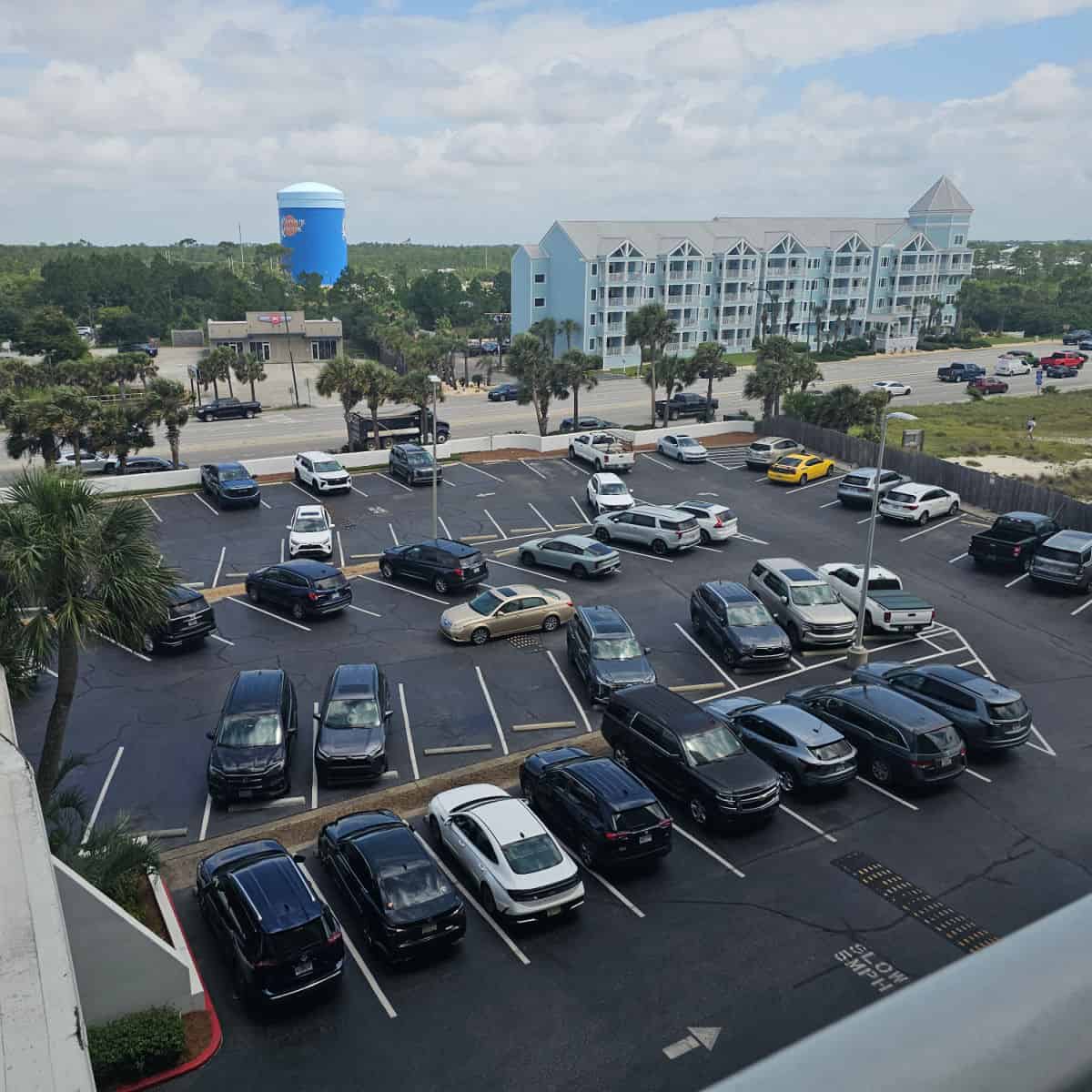 looking down over a paved parking lot with cars, Orange Beach water tower in the background and a blue multi-story condo building