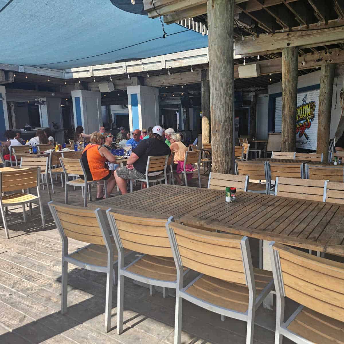 outdoor seating with people under a cover, large harpoon harry's logo in the backgorund