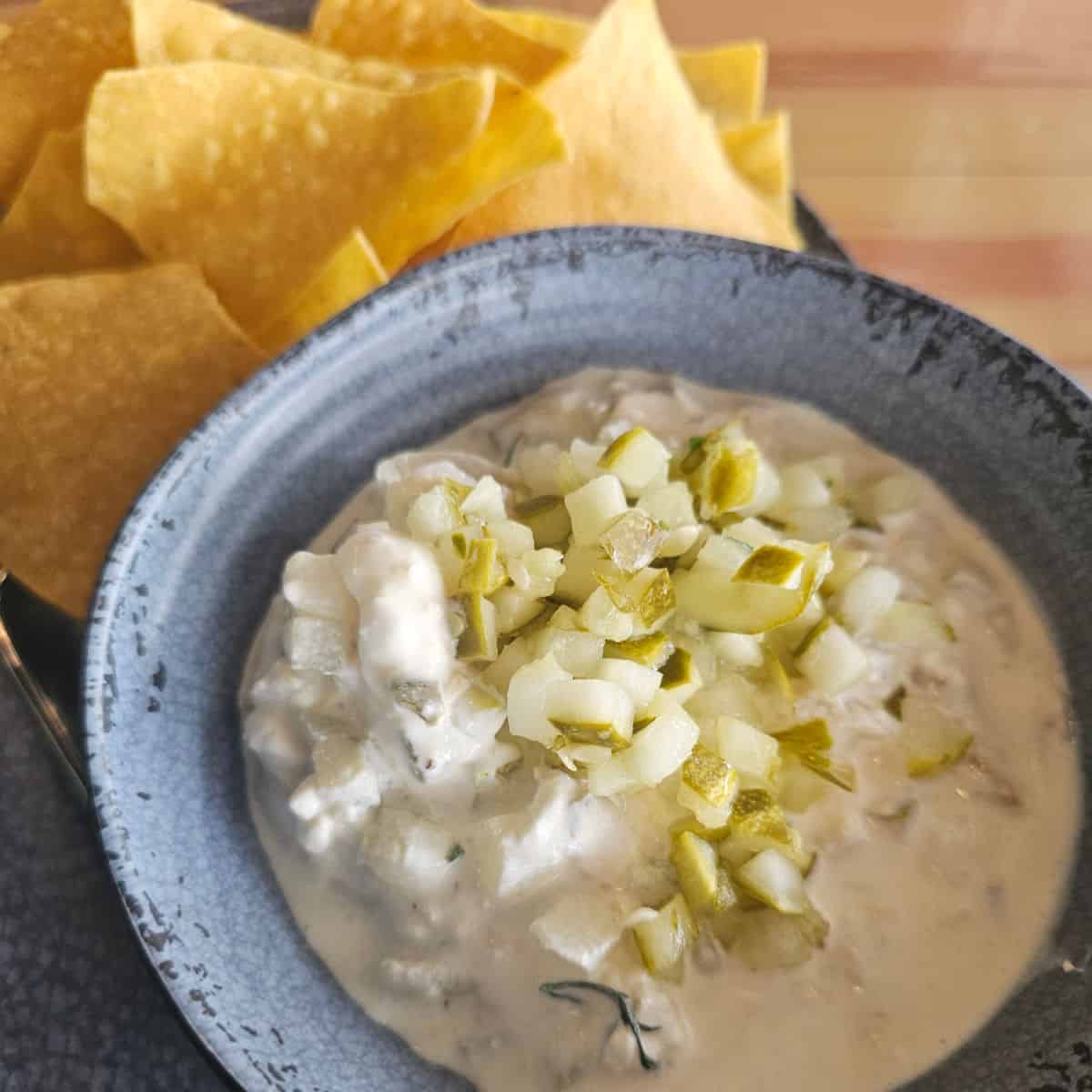 pickle dip in a blue bowl with chips next to it.