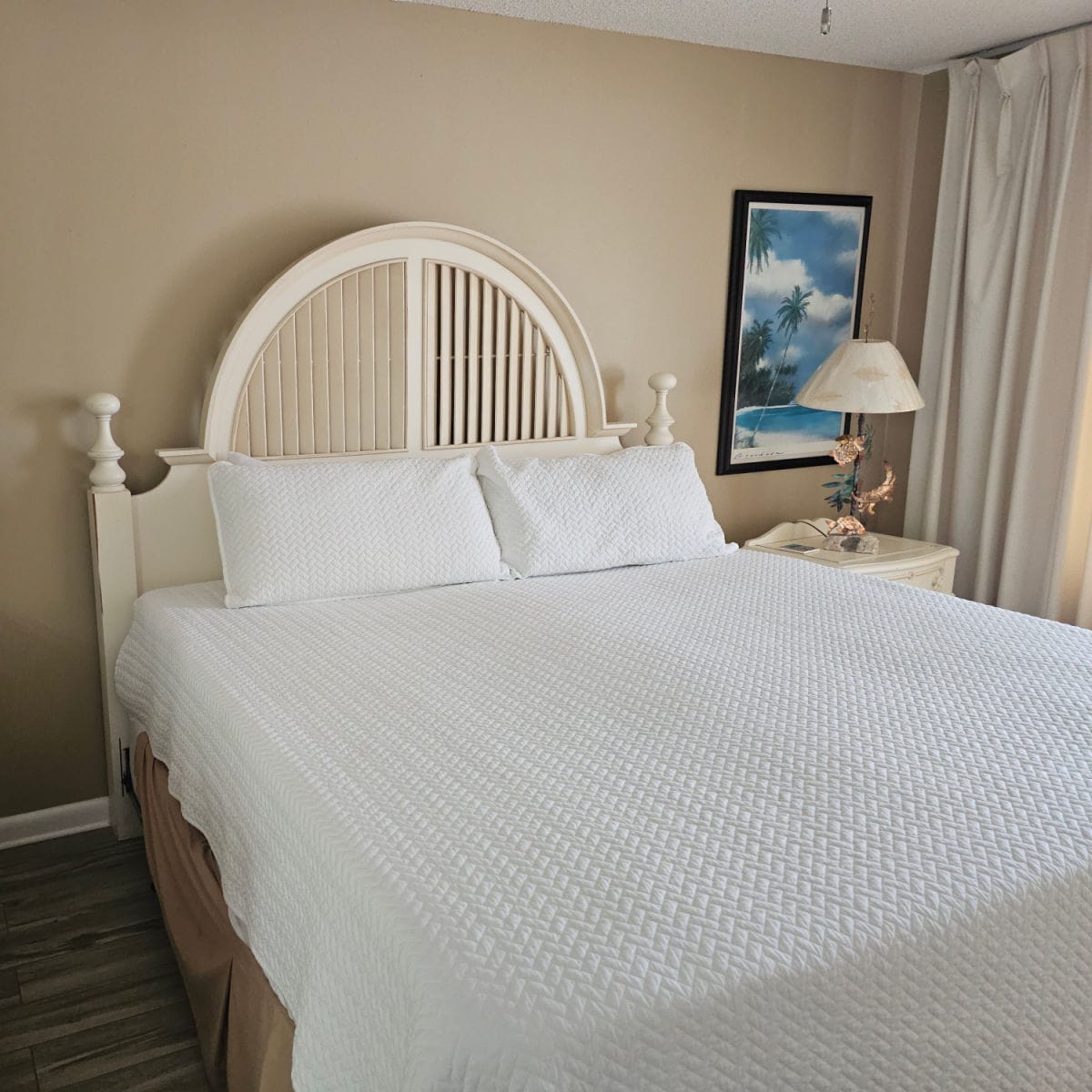 bedroom with brown walls, bed with wooden bedframe, nightstand with ornate lamp, and tropical poster on the wall