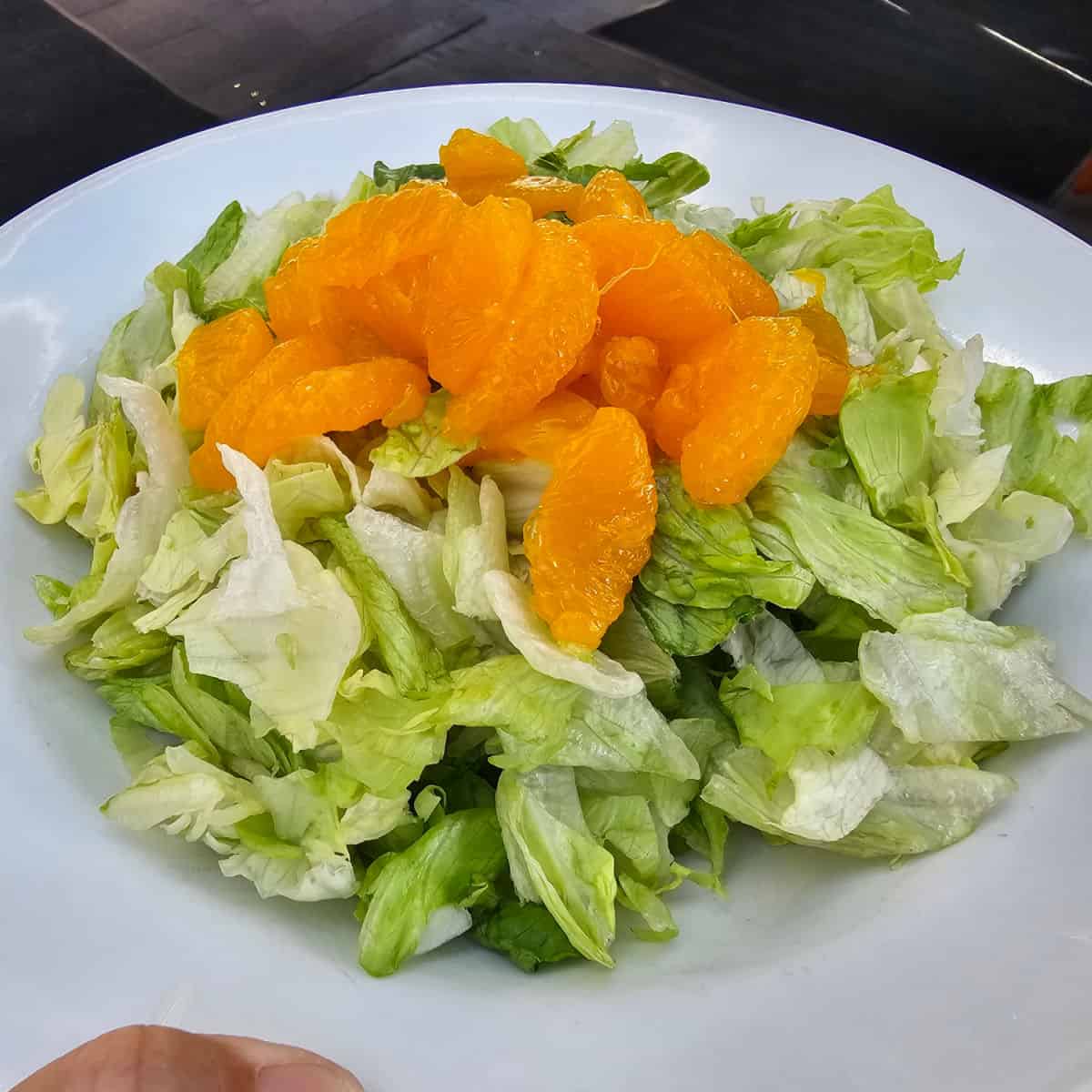 salad with orange slices on the top of it in a white bowl