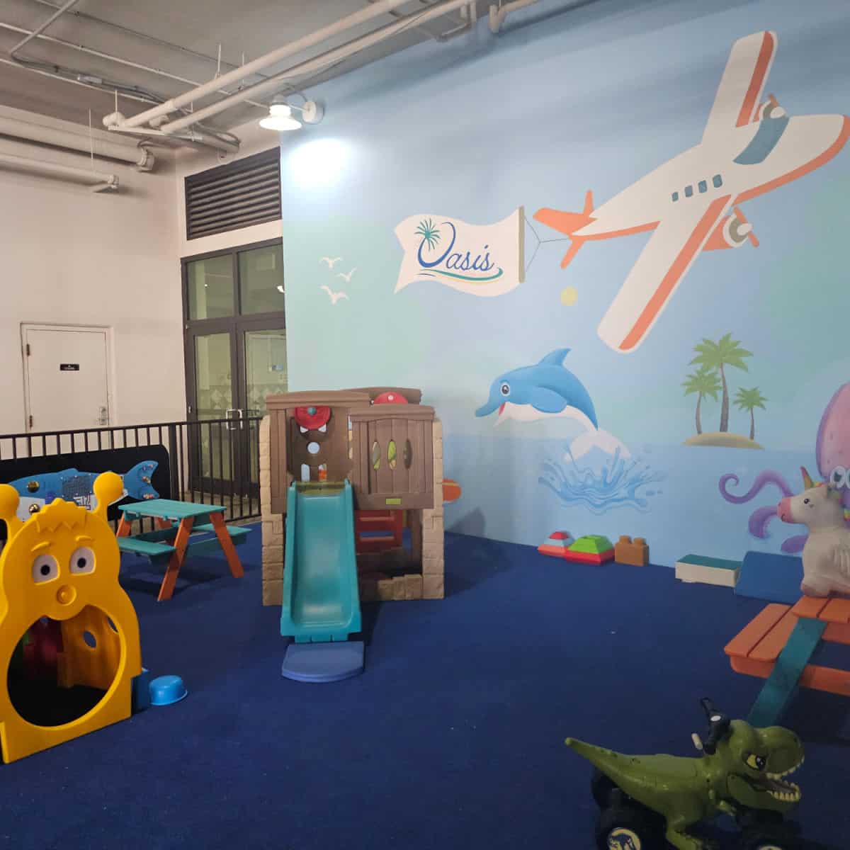 Kids play area with a plane mural on the all pulling an Oasis sign, dolphin jumping out of the water. Kids play tous and table spread out with other blocks and games