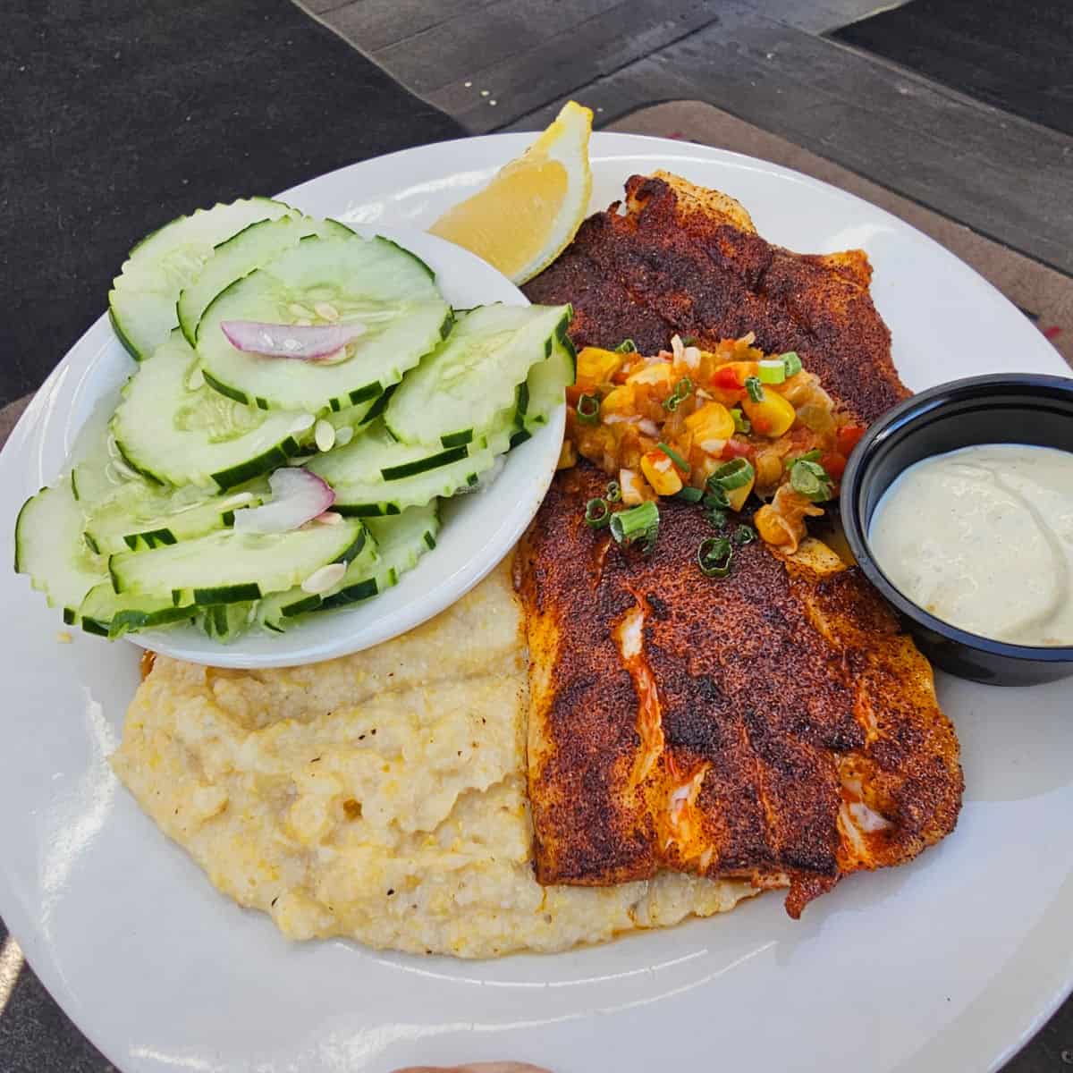 blackened fish on a white plate with cucumbers and grits