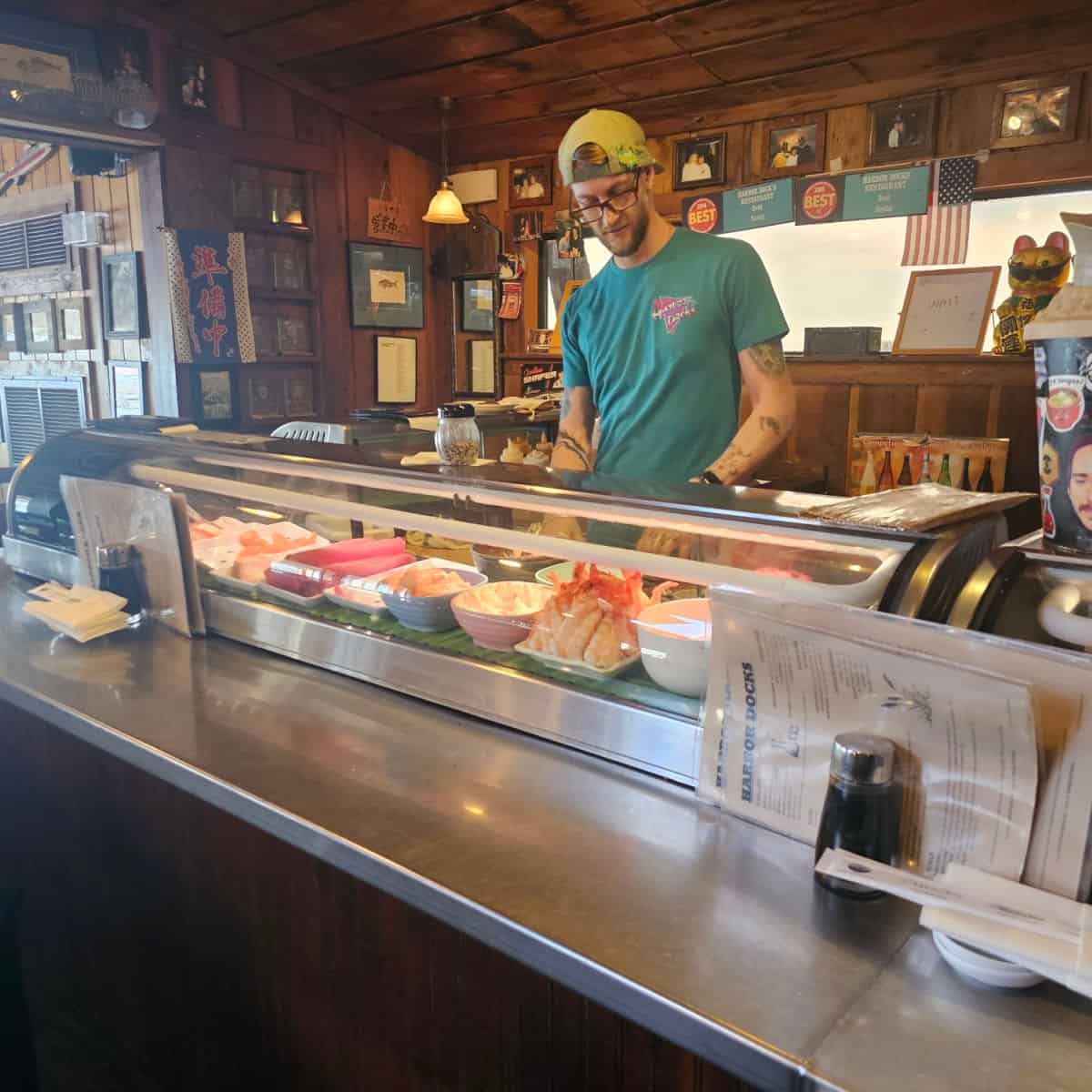 sushi counter with fresh fish under a glass cover, chef working on preparing sushi at Harbor Docks