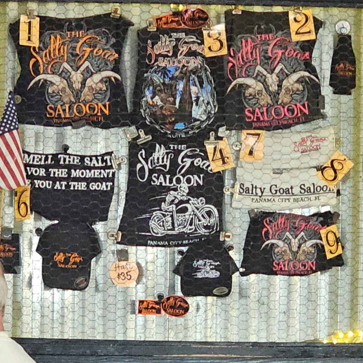 Salty Goat Saloon t-shirts with number tags hanging behind chicken wire