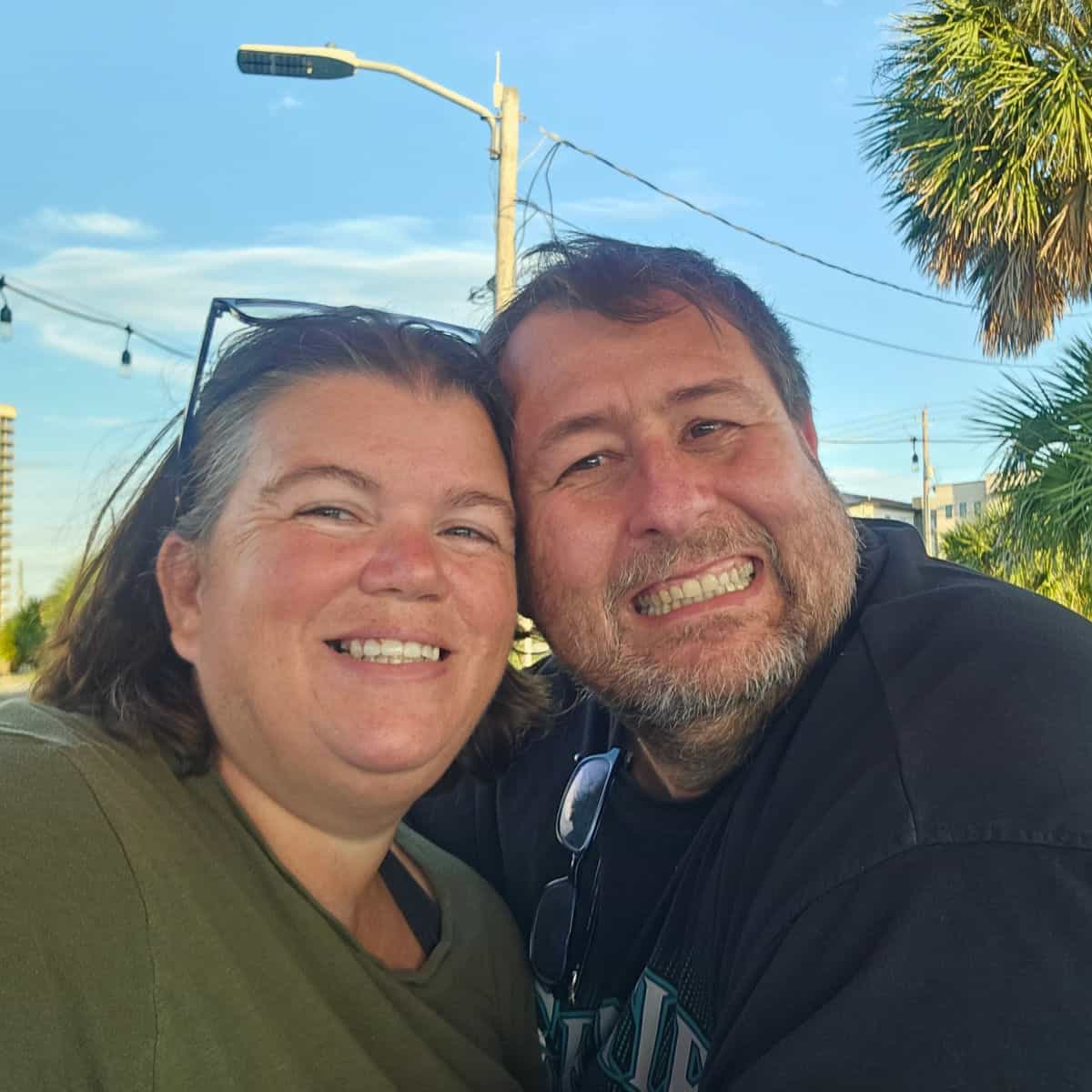 tammilee and john smiling with a palm tree behind them