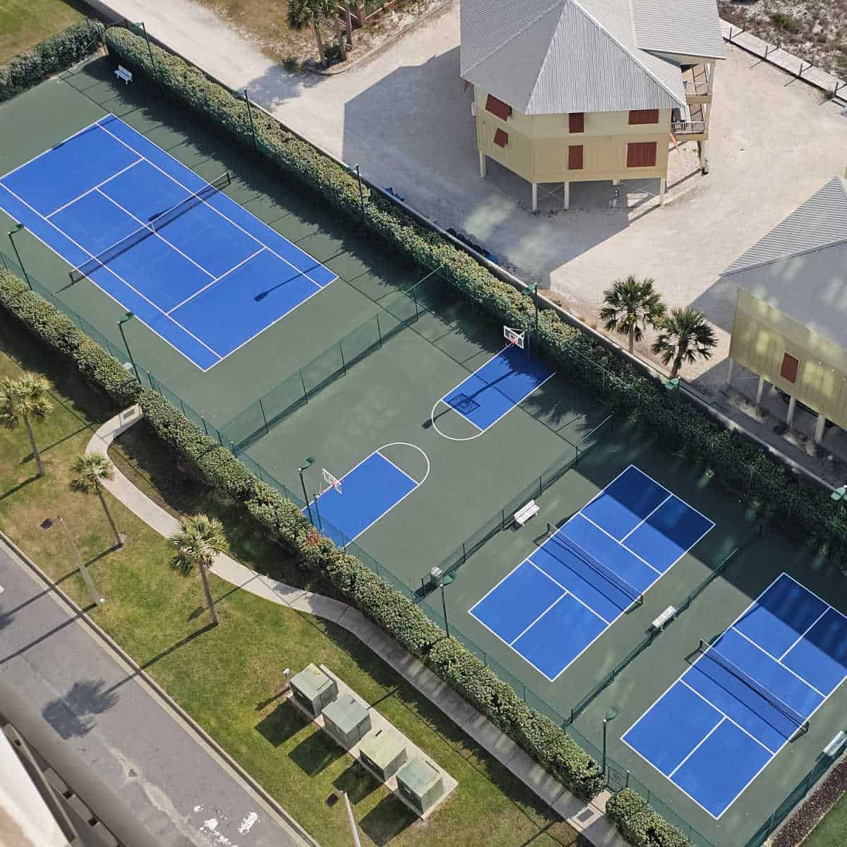 Looking down over tennis, pickleball and a basketball court surrounded by tall shrubs