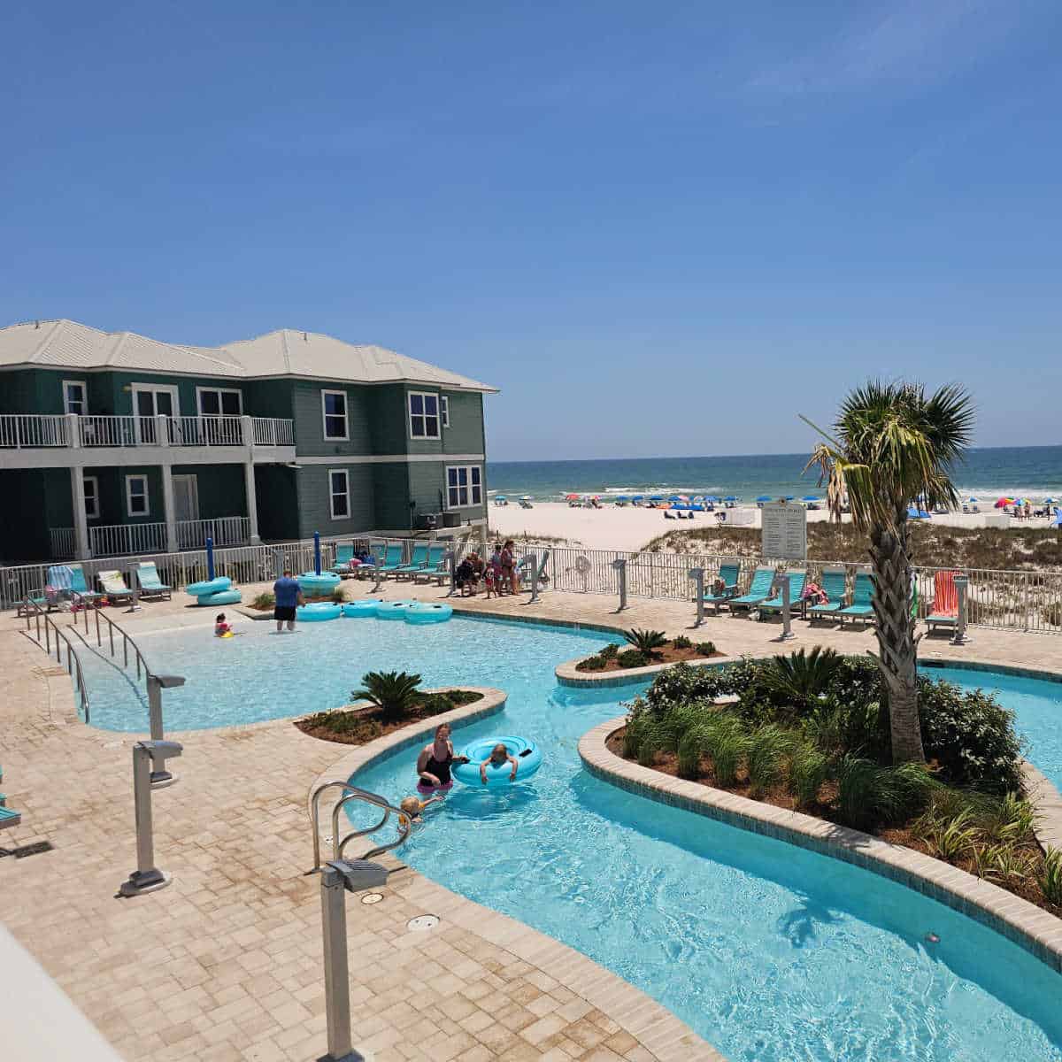 Zero entry pool leading to a lazy river with turquoise intertubes, lounge chairs around the pool deck, looking out towards the beach and Gulf waters