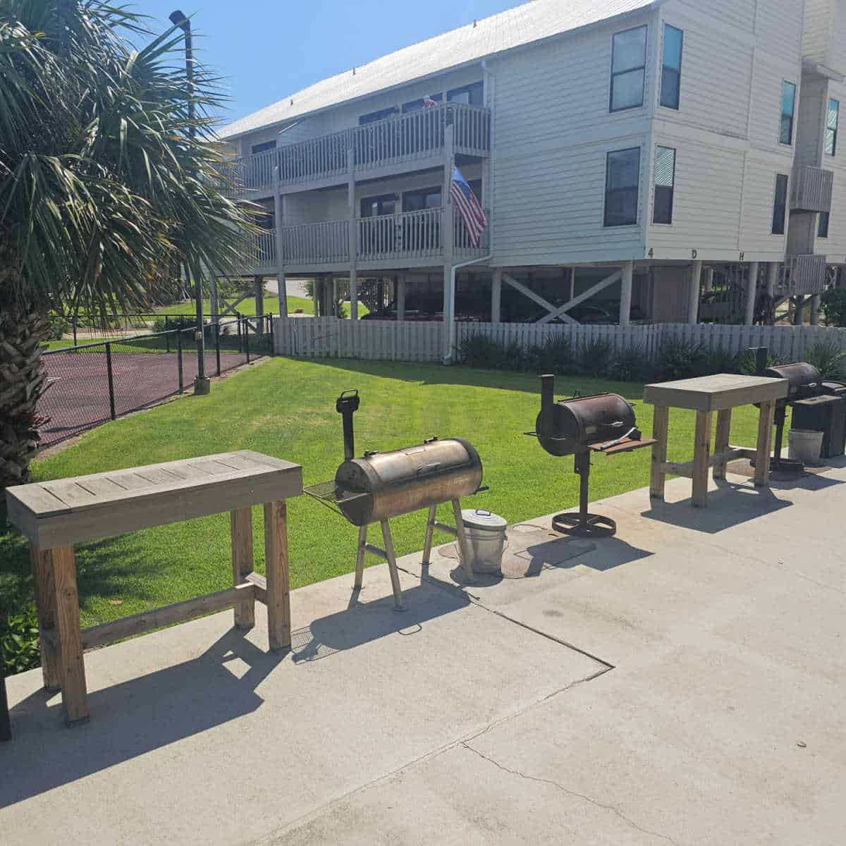 bbq area with multiple charcoal grills and wooden prep tables in between the bbq's