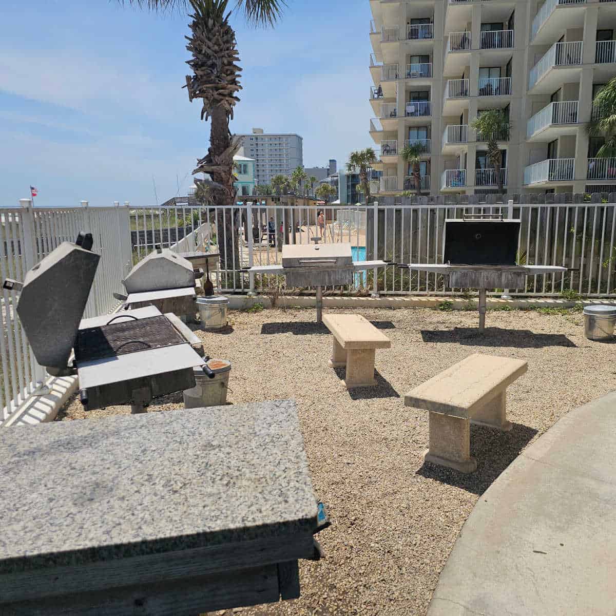 outdoor charcoal barbecues along a fence with concrete benches and tables nearby
