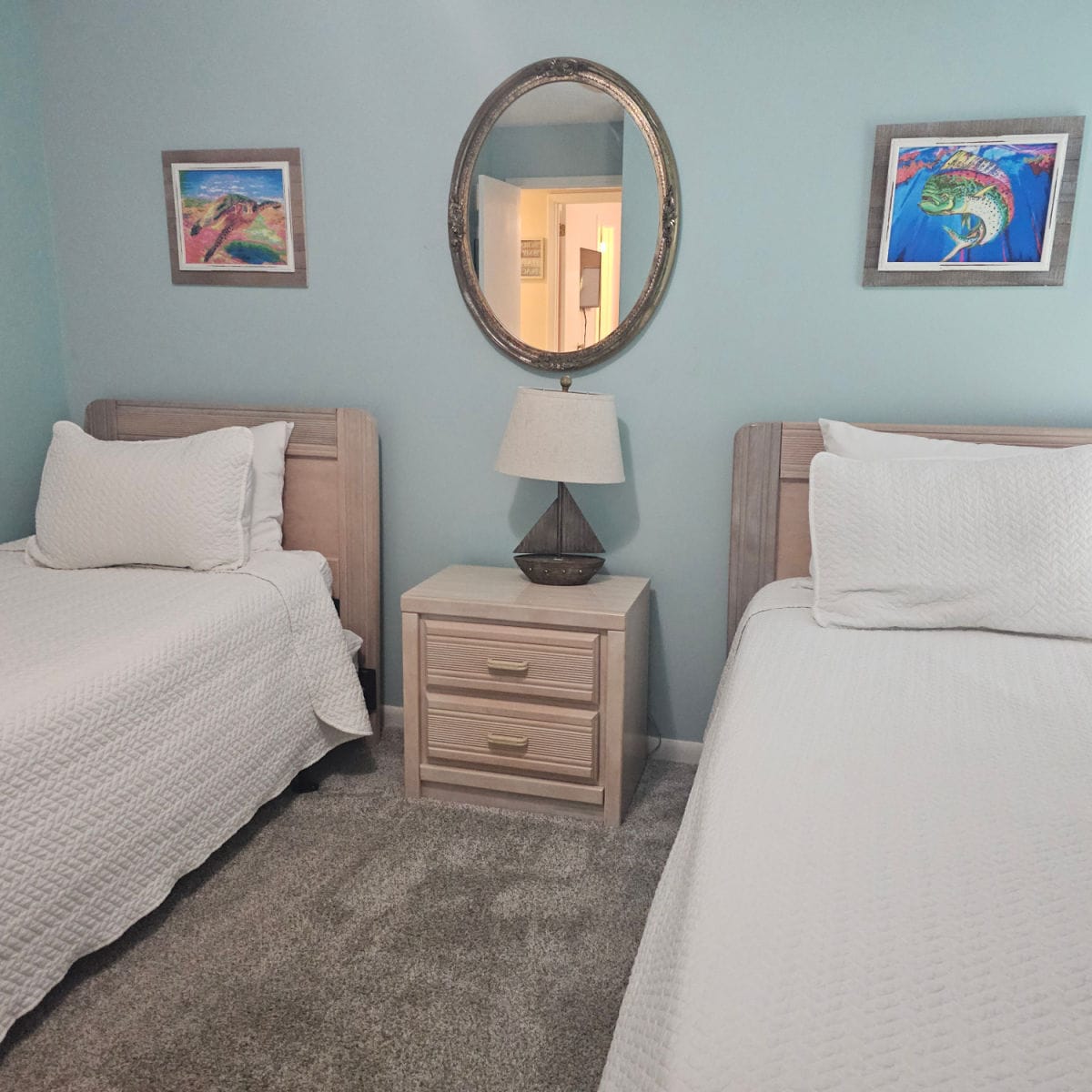 Bedroo with two beds, nightstand between the bed with a sailboat lamp, mirror above the lamp, fish prints over the beds
