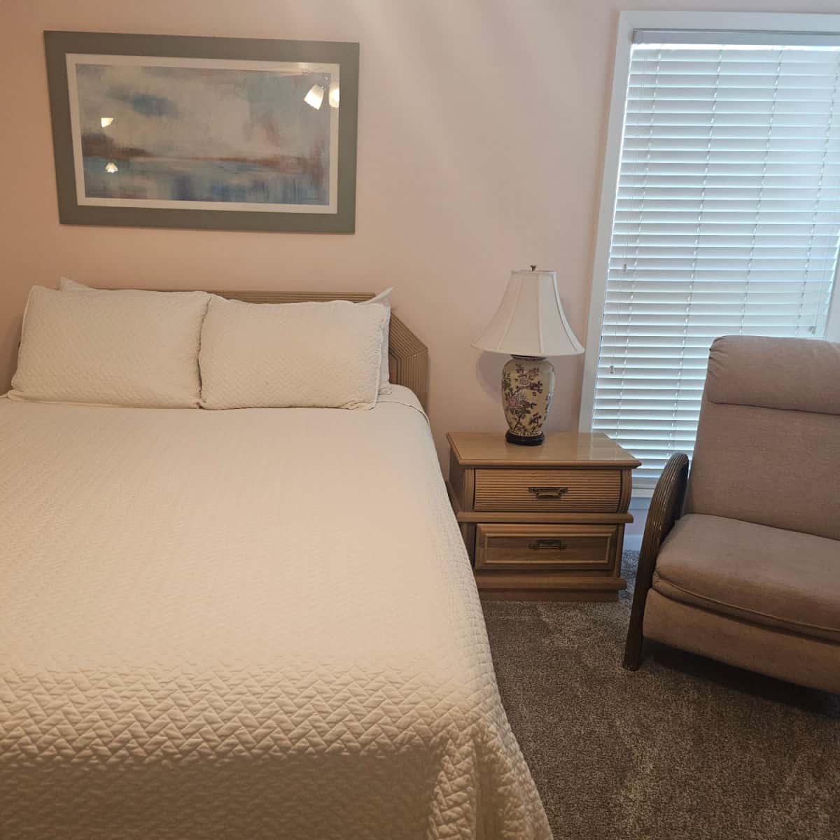 bedroom with a bed, wooden nightstand with a lamp on it, brown chair, and art over the bed
