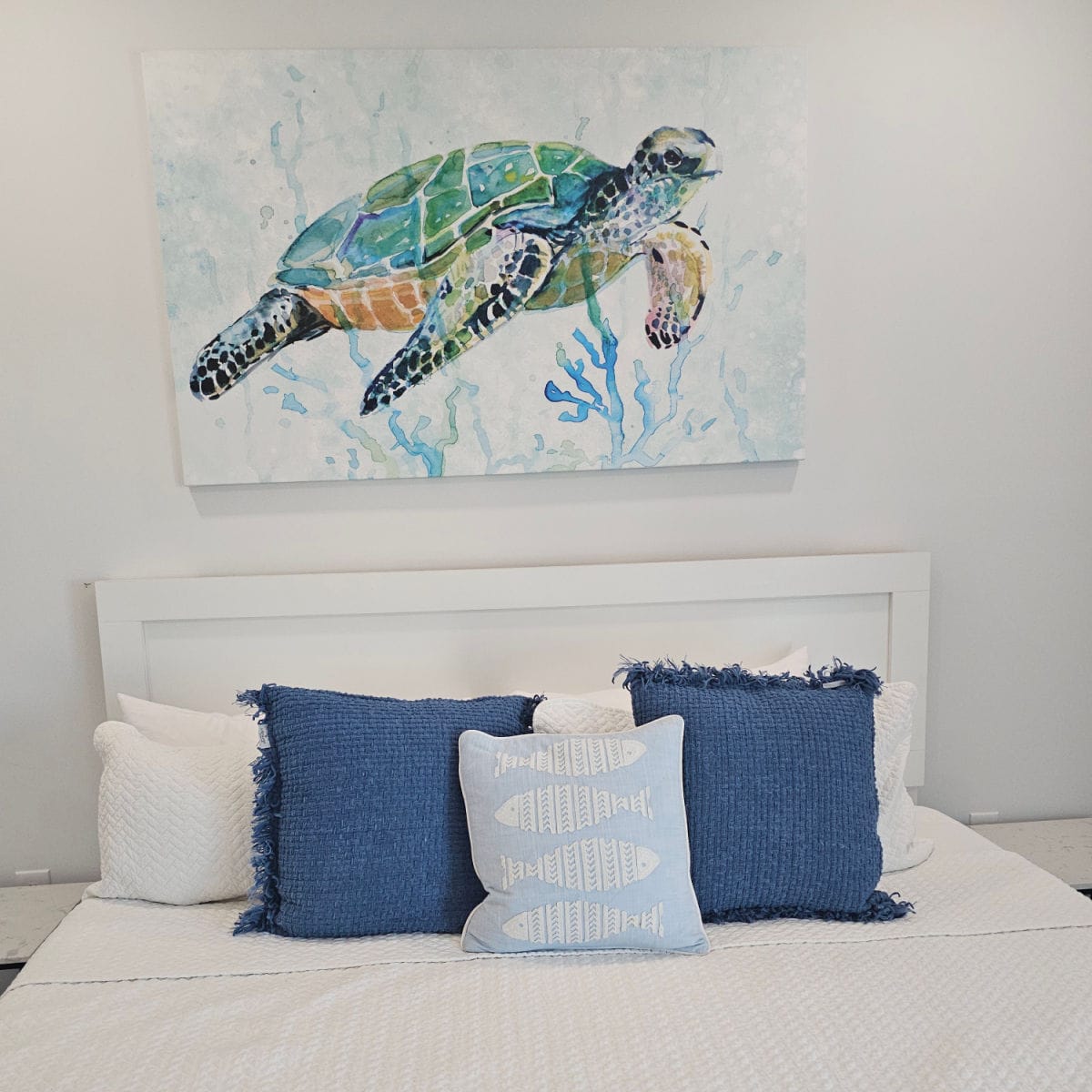 Bedroom with white linen covered bed with blue pillows, turtle art over the bed