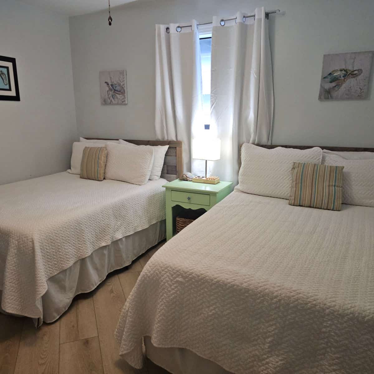 Bedroom with two beds, green nightstand between the beds, turtle photos on the walls