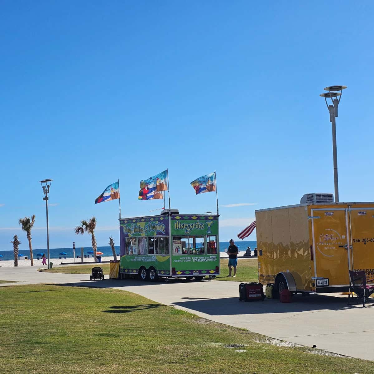 two food trucks lined up with the Gulf and Palm trees in the background