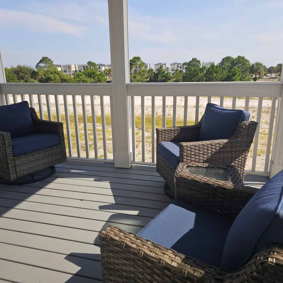OUtdoor seating on a deck with wicker chairs and blue covers looking out towards tall trees and buildings