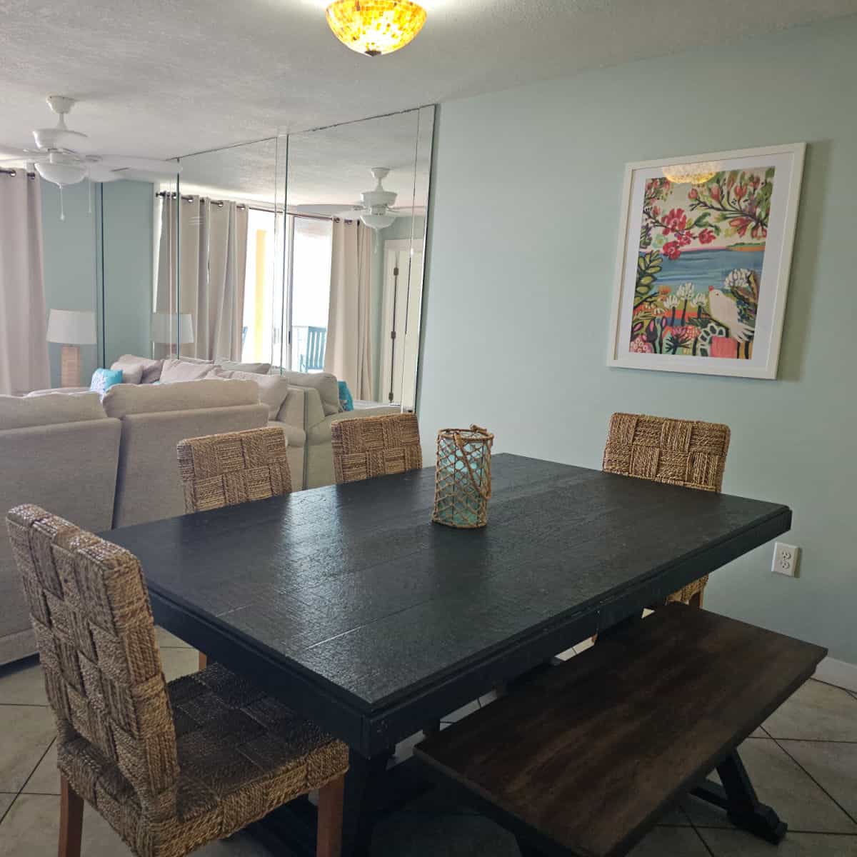 Dining room table with chairs, coastal art print on the wall, mirror wall and couches to the left