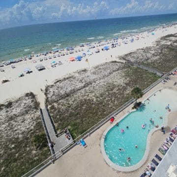 looking over a large outdoor pool to boardwalks over the sand dunes to the white sand beach and Gulf waters