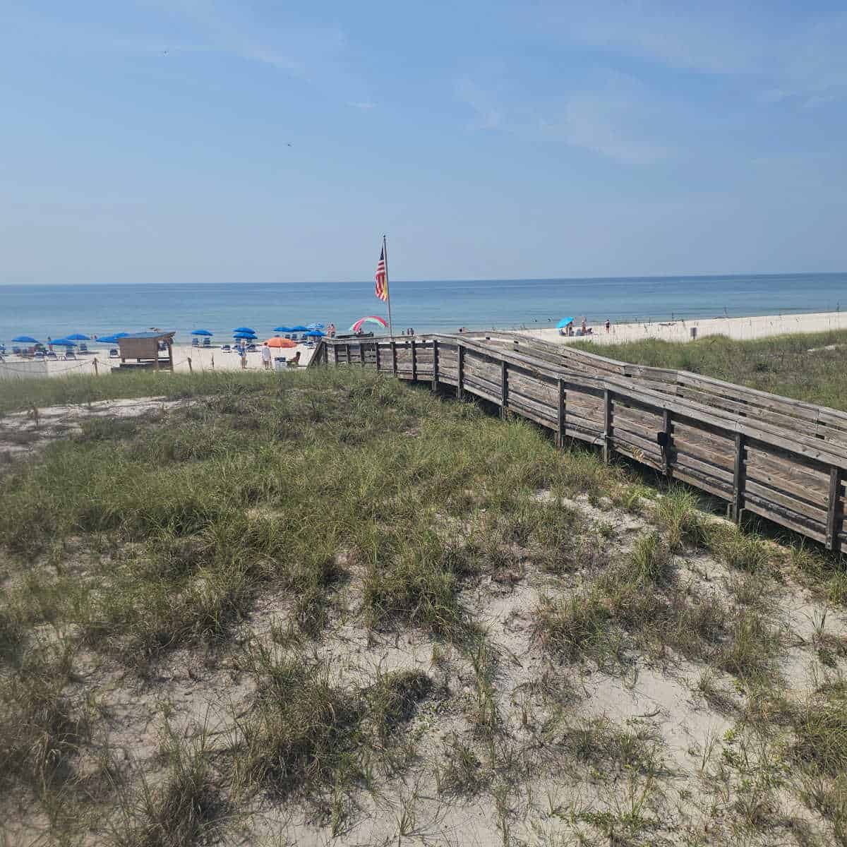 wooden boardwalk over sand dunes leading to white sand beach and Gulf waters.