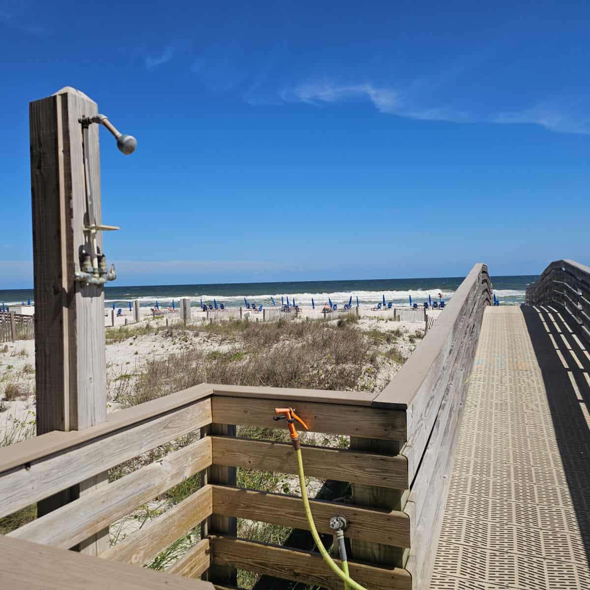 beach access boardwalk with an outdoor shower on the side. Gulf waters and white sand beach in the background