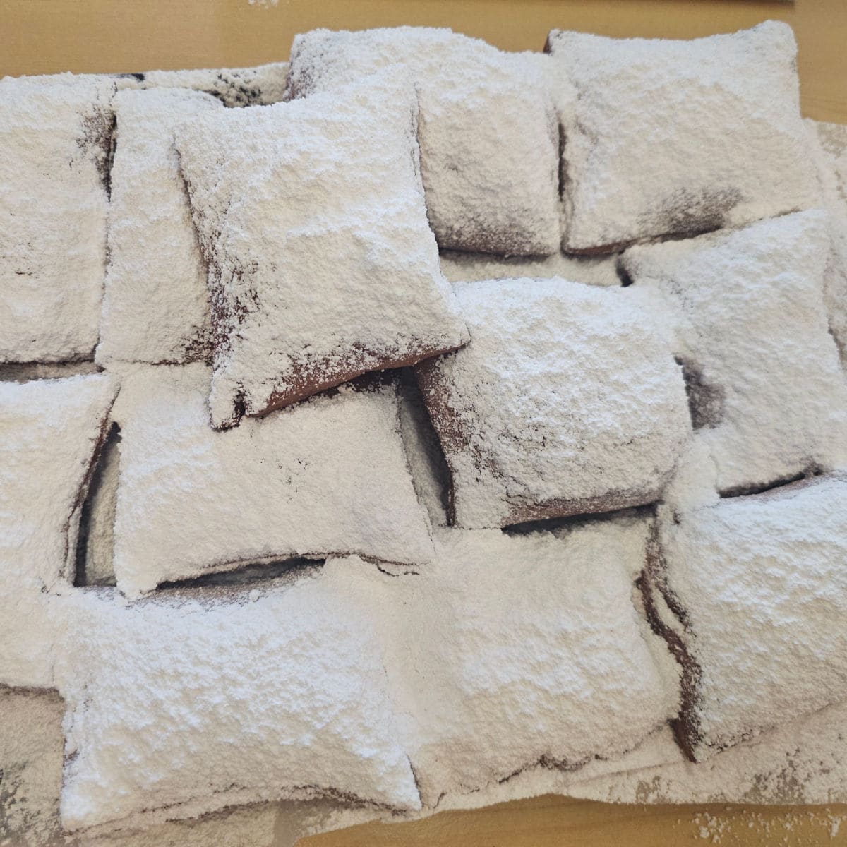 A dozen powdered sugar covered beignets on a tray