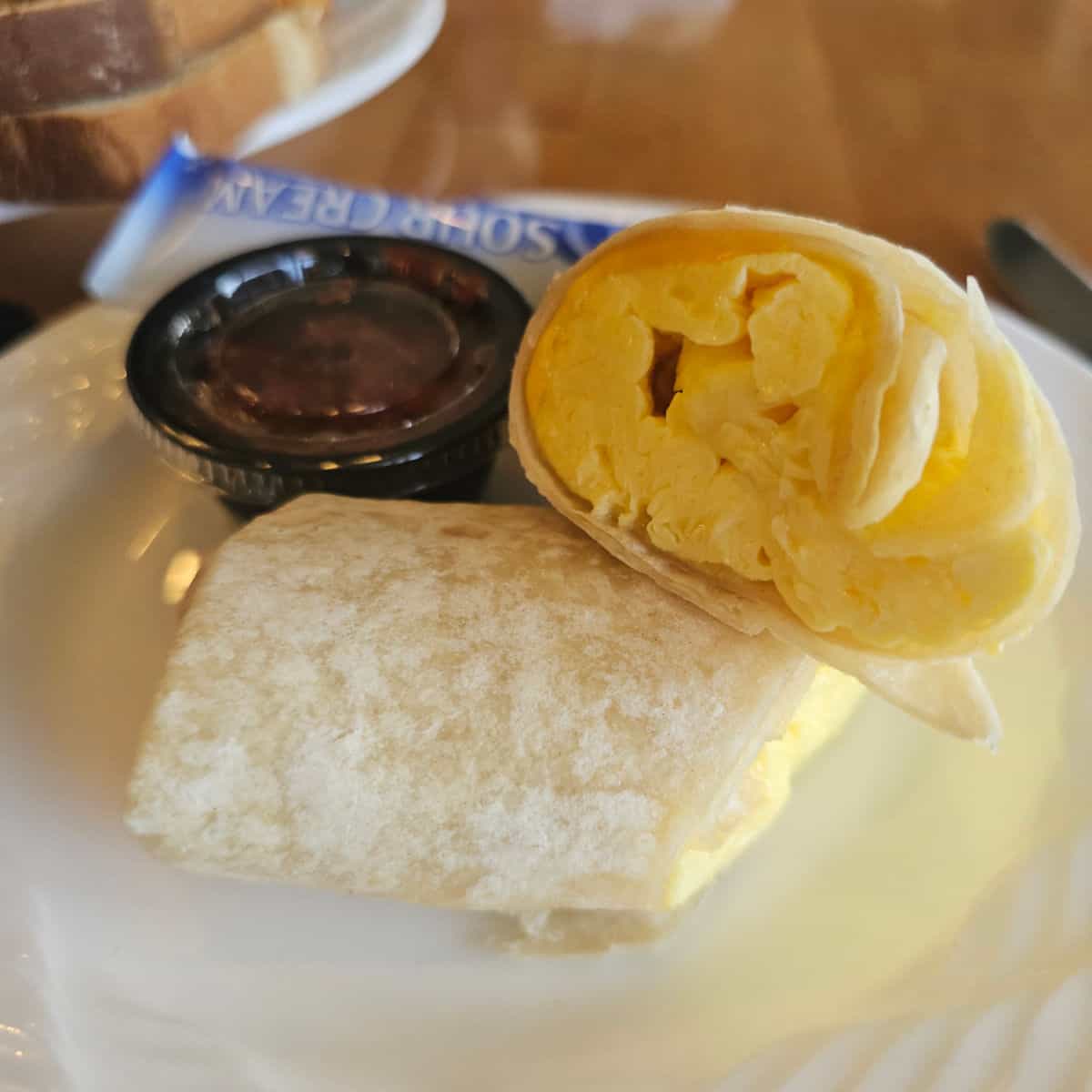 egg and cheese breakfast burrito on a white plate with a container of salsa and sour cream