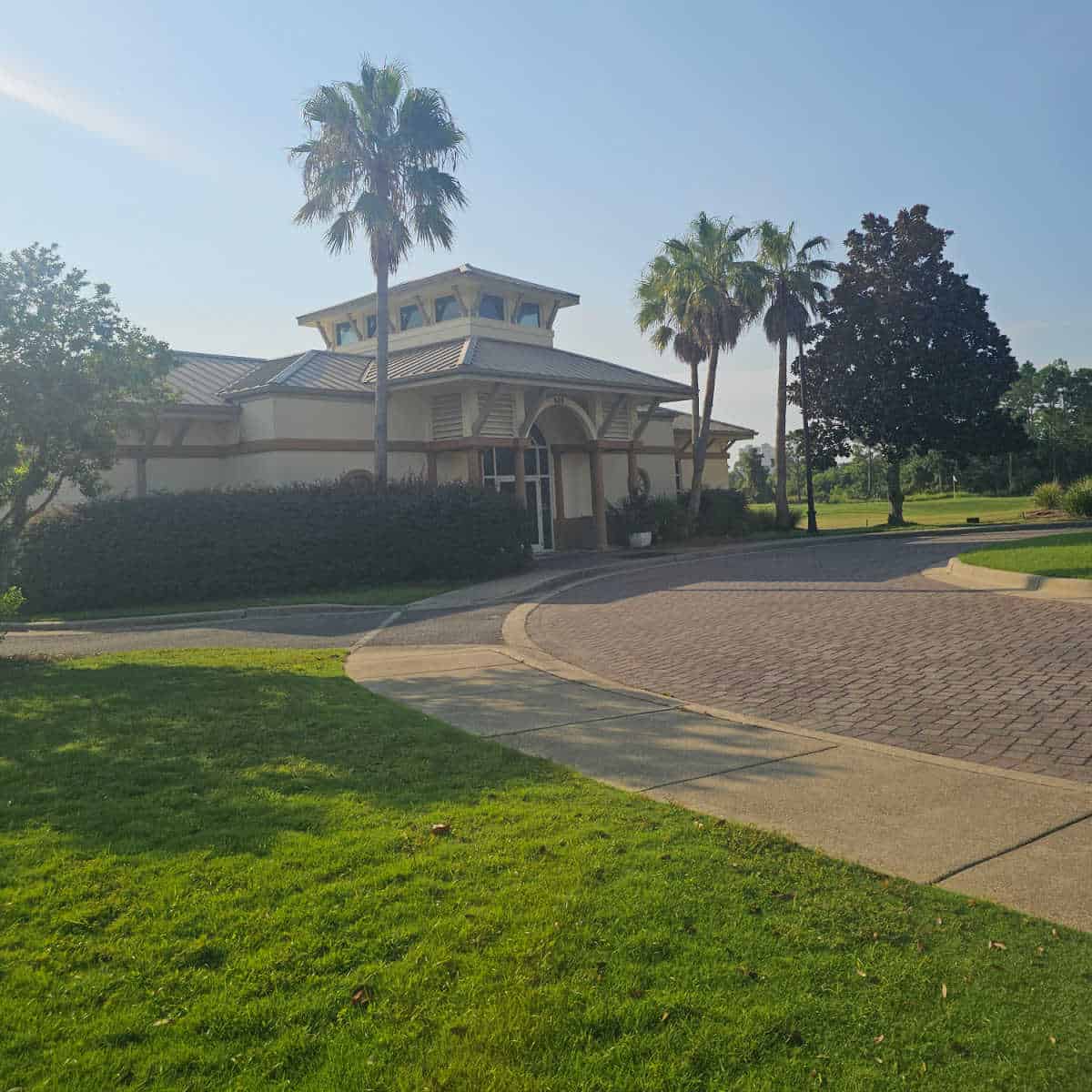 walkway up to Lost Key Golf Clubhouse with palm trees and single story tan building golf course in the background
