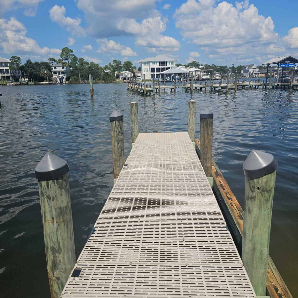 fishing dock out over the water with a boat dock in the background and houses across the water.