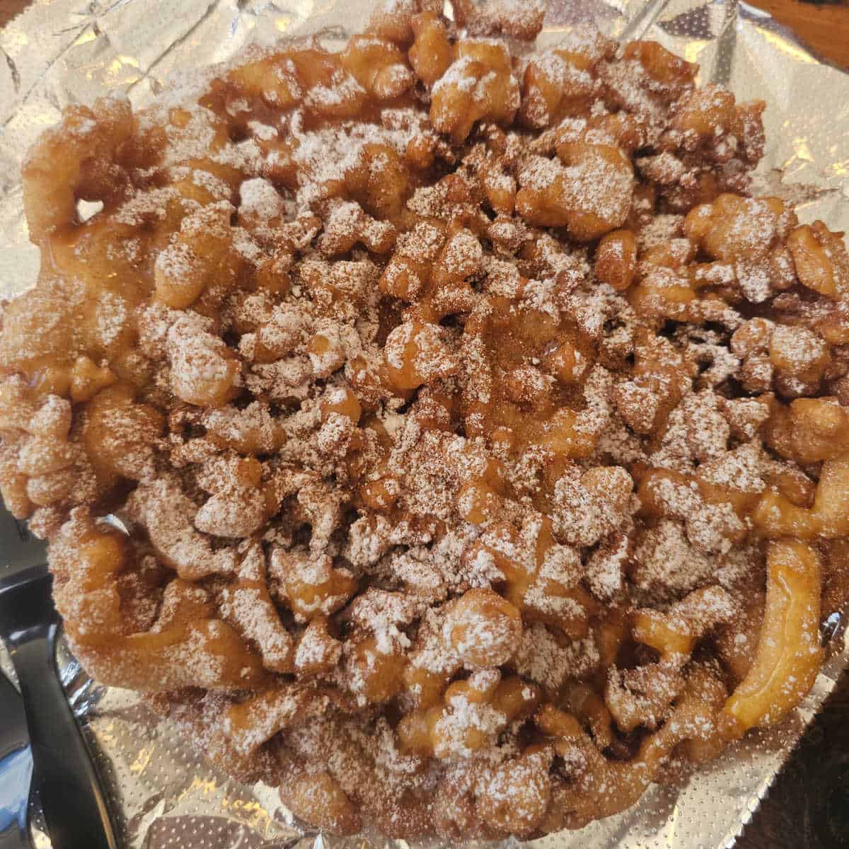 Funnel cake topped with powdered sugar on a piece of foil