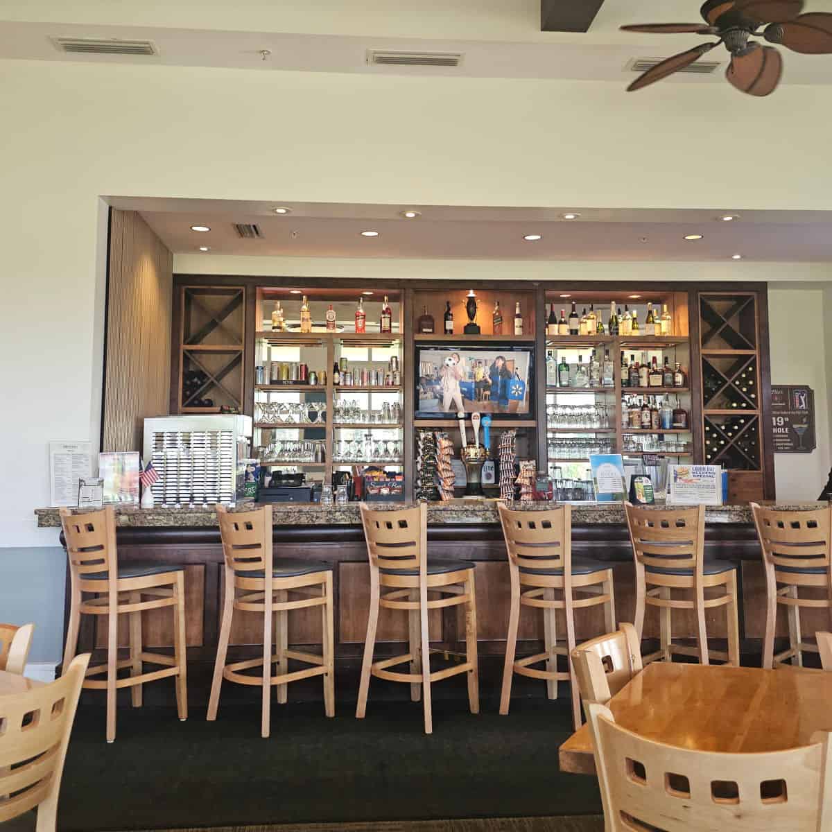 indoor bar with tall stools up against the bar, shellves of bottles and glasses with a tv in the middle