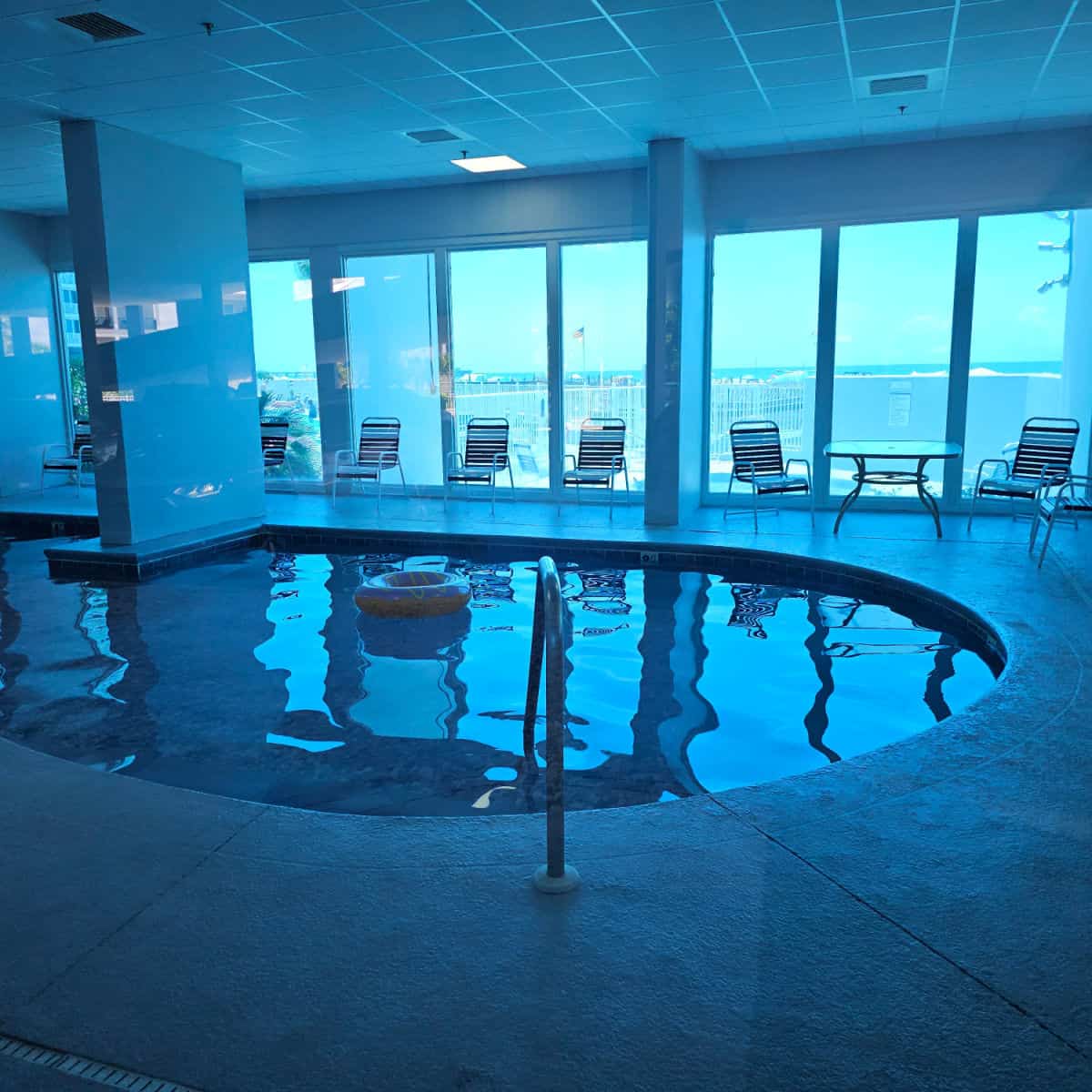 Indoor swimming pool with deck chairs around the deck, looking out the window towards the beach and Gulf