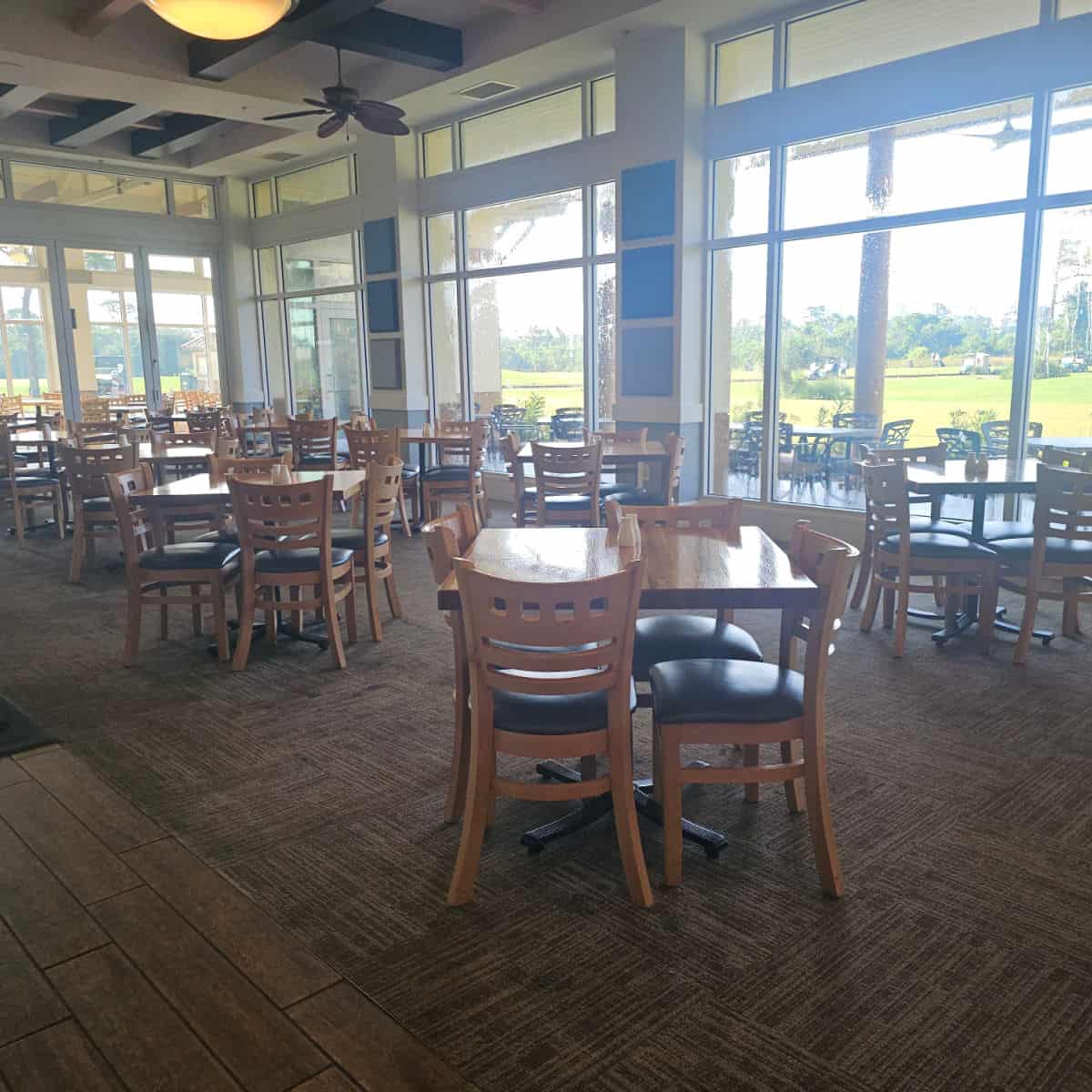 indoor seating with tables and 4 chairs around each table, looking out the window towards a golf course