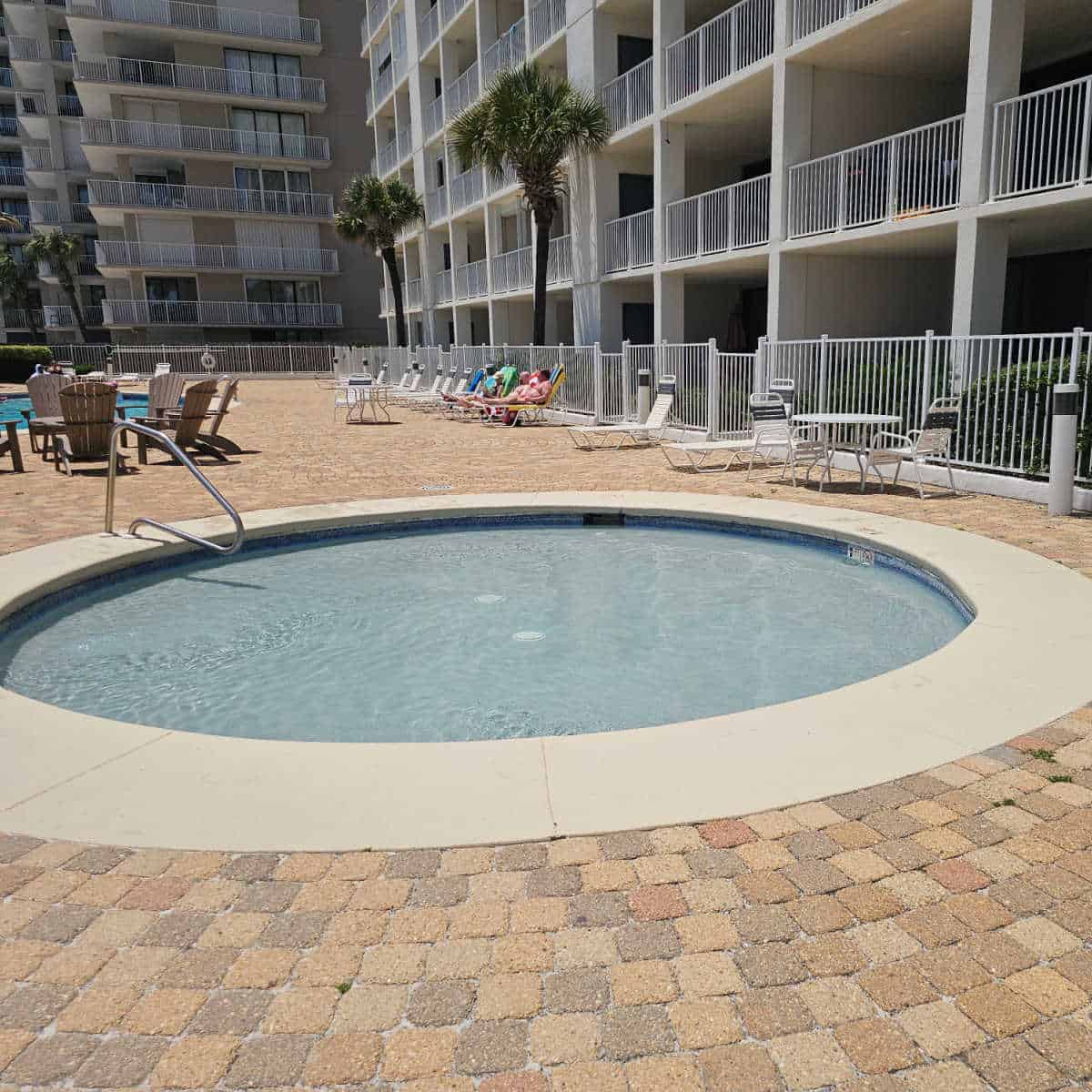 large circular kiddie pool with lounge chairs along the pool deck and condo building next to the fence