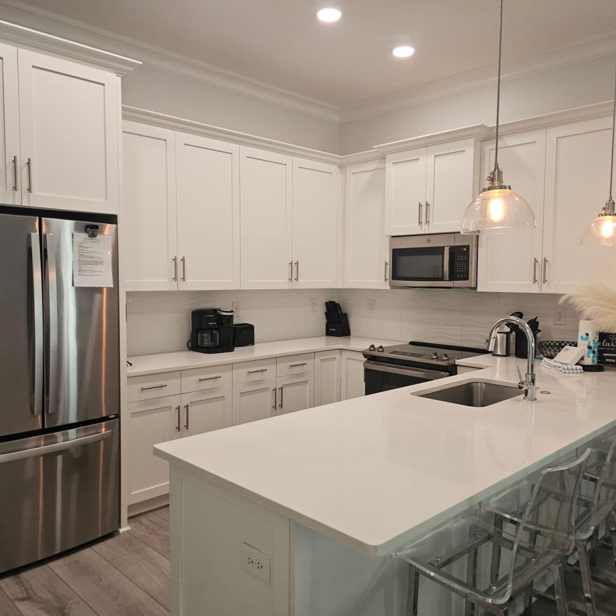 Kitchen with white cabinets, stainless steel appliances, and stools up against the counter